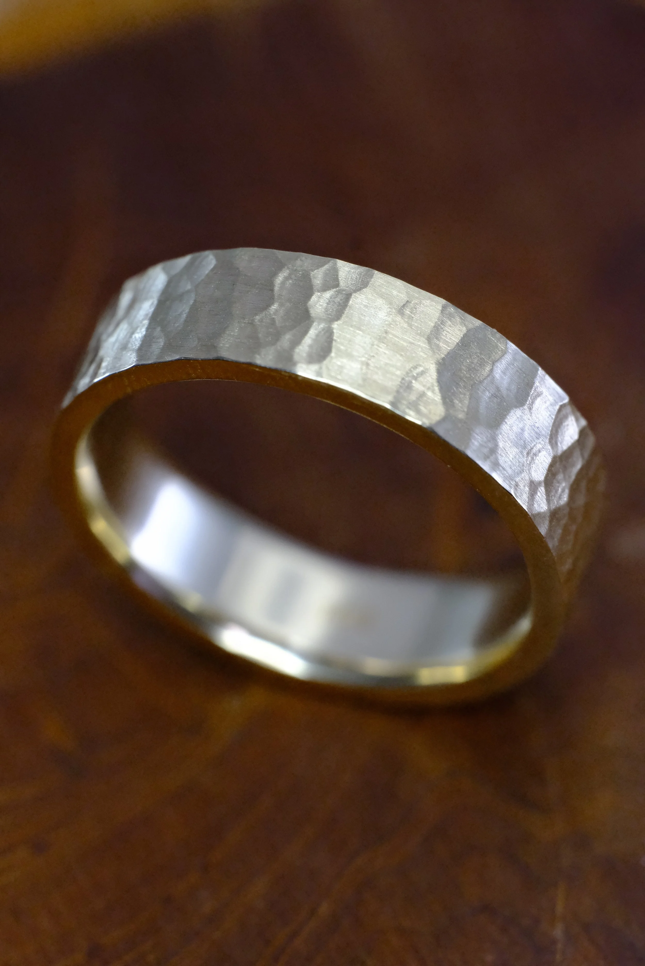 Yellow gold men’s band with hammered finish and matte texture, shown at an angle on a wooden surface.