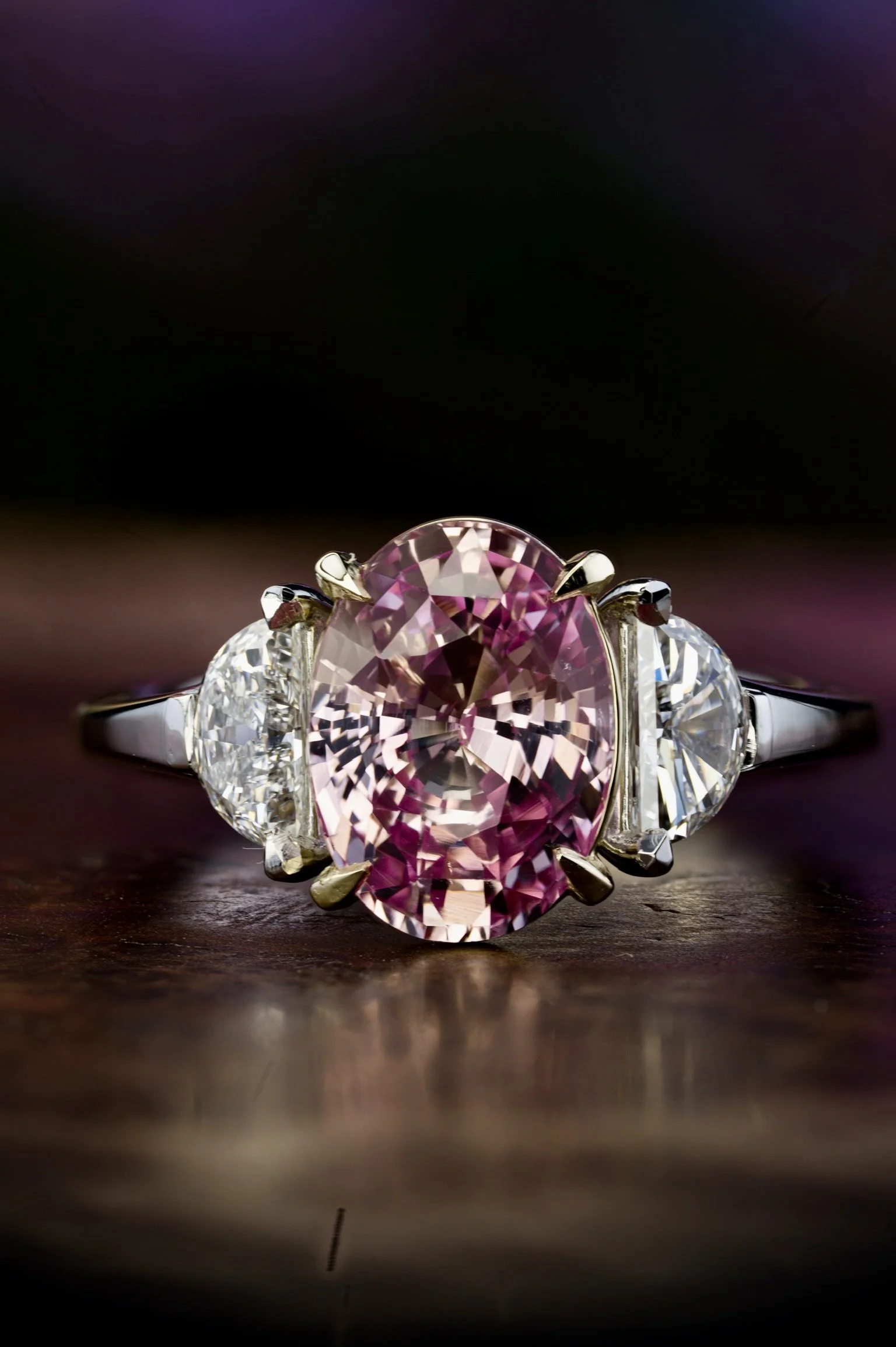 Two-tone platinum and yellow gold ring with oval pink center stone and two side diamonds, shown head-on.