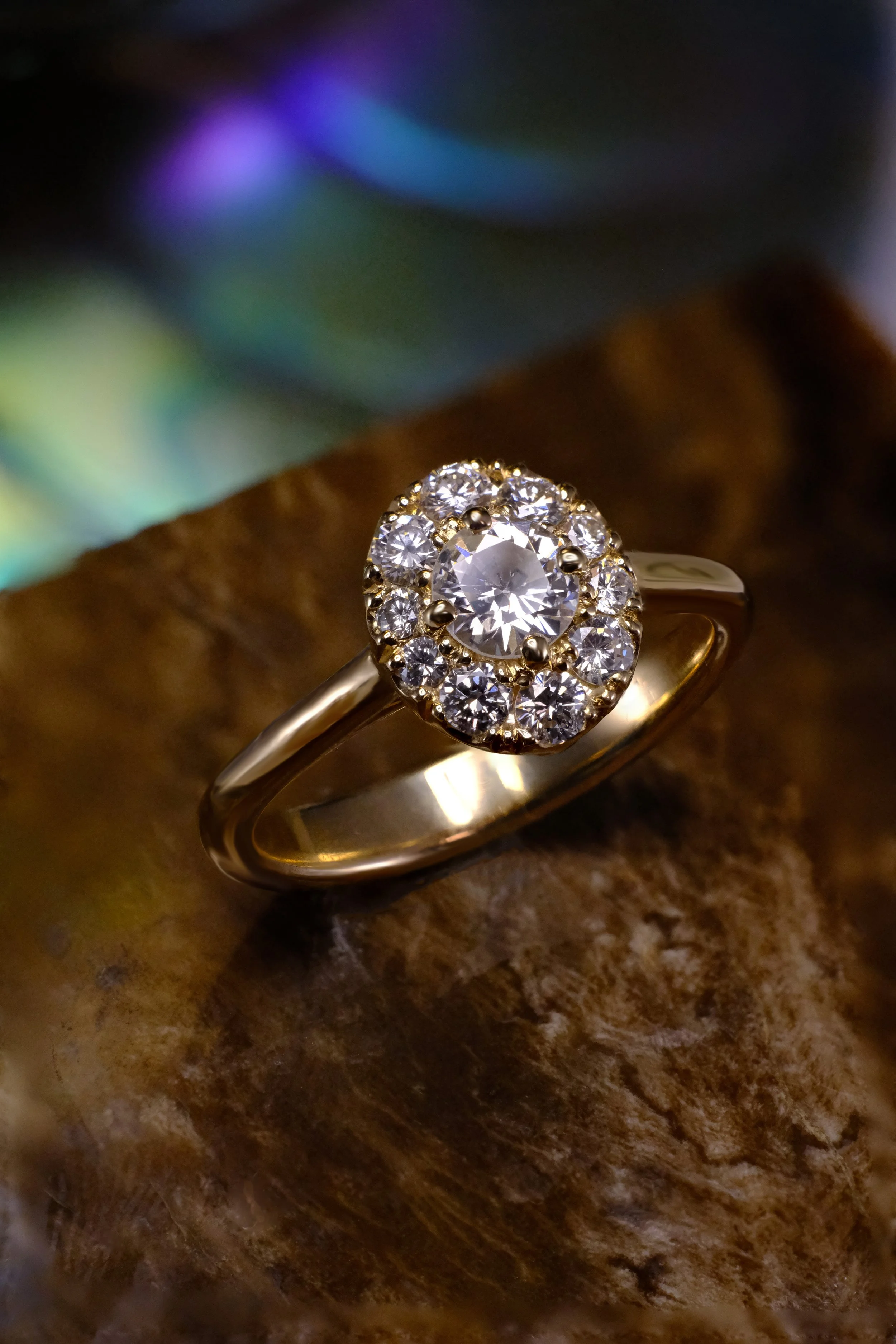 Yellow gold ring with a round center diamond surrounded by a graduated halo of round diamonds, shown at a slight angle on a textured surface.
