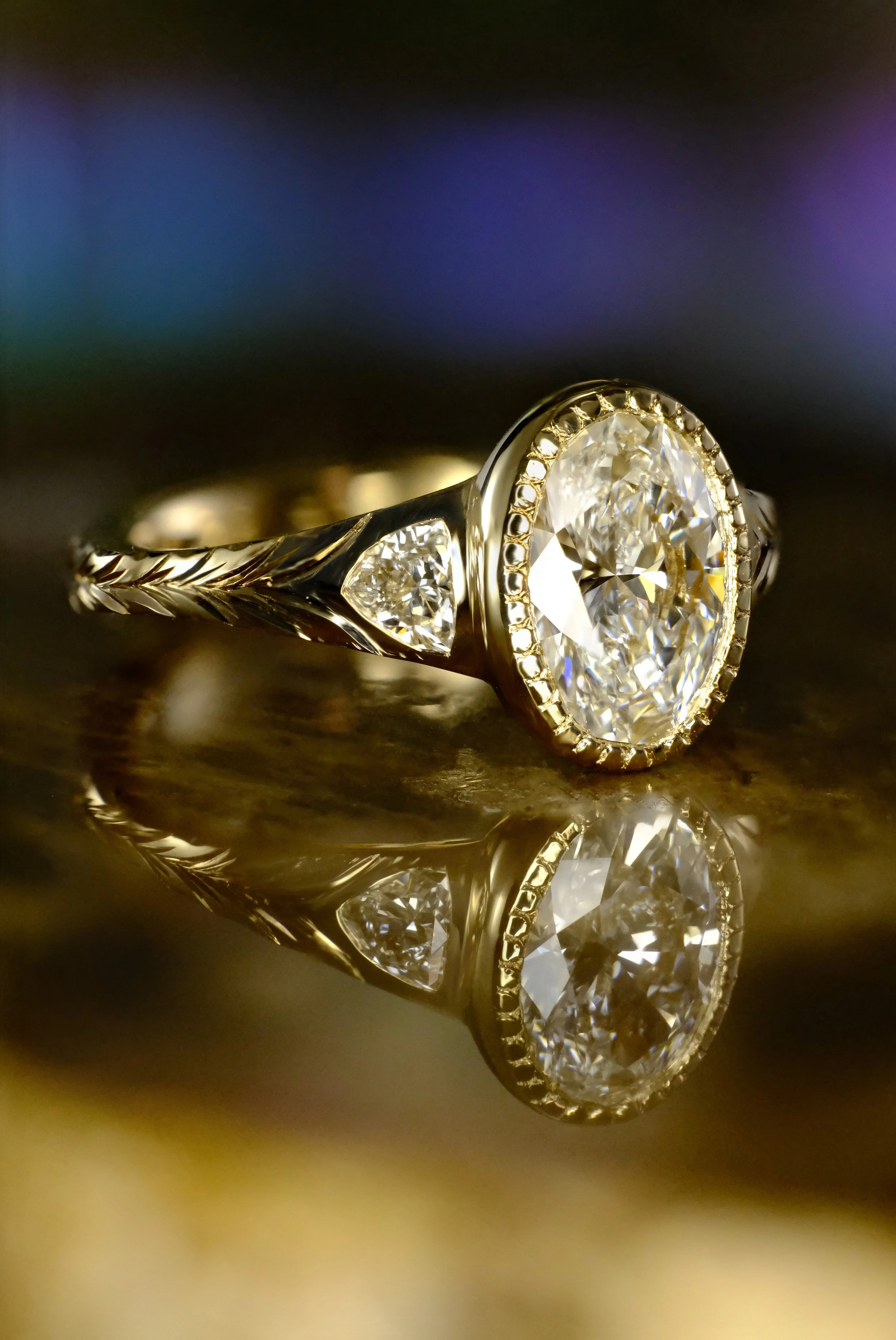 Yellow gold ring with oval diamond in bezel setting and engraved band, shown from the side highlighting details.