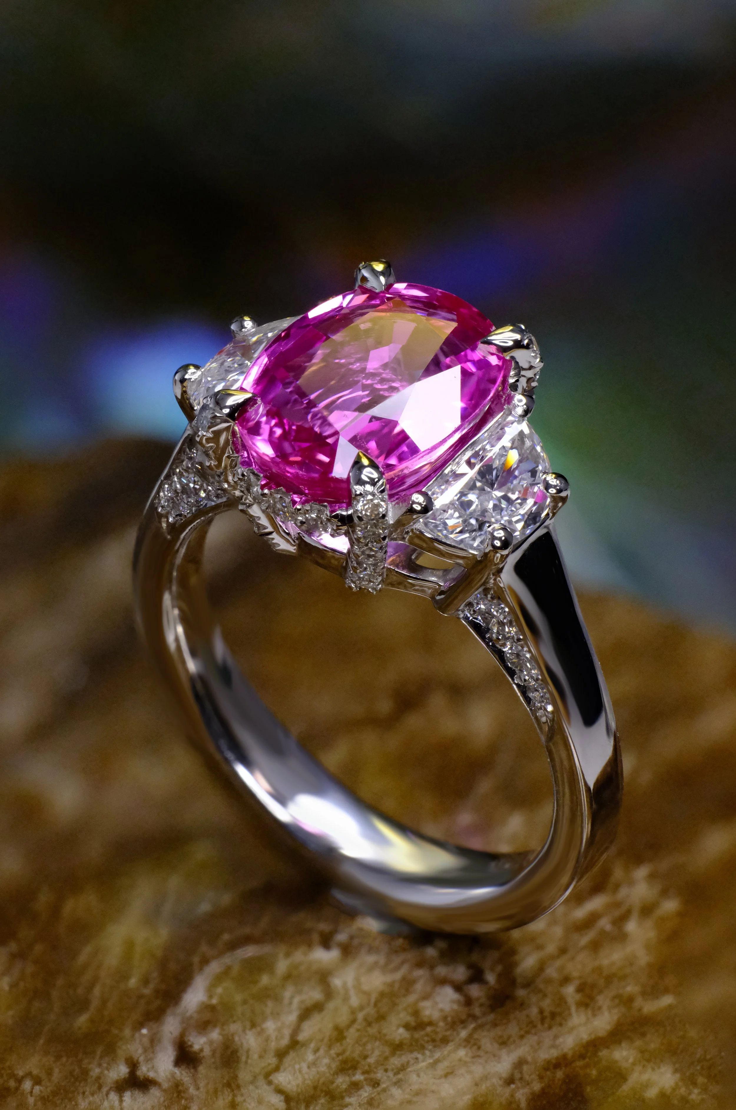 Platinum ring with oval pink gemstone, diamond side stones and pavé accents, shown from the side.