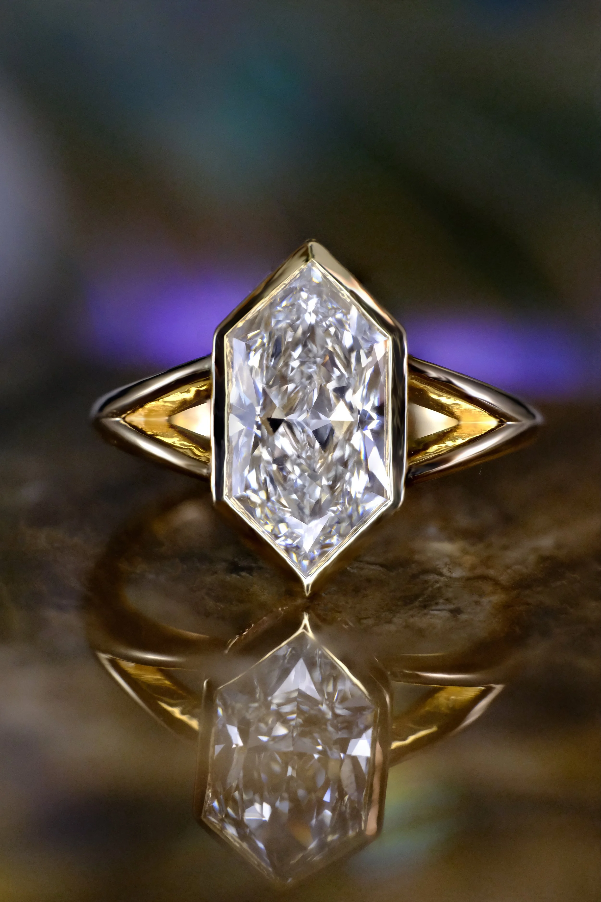Yellow gold ring with marquise diamond in bezel setting, shown head-on with centered stone and reflection on a glossy surface.