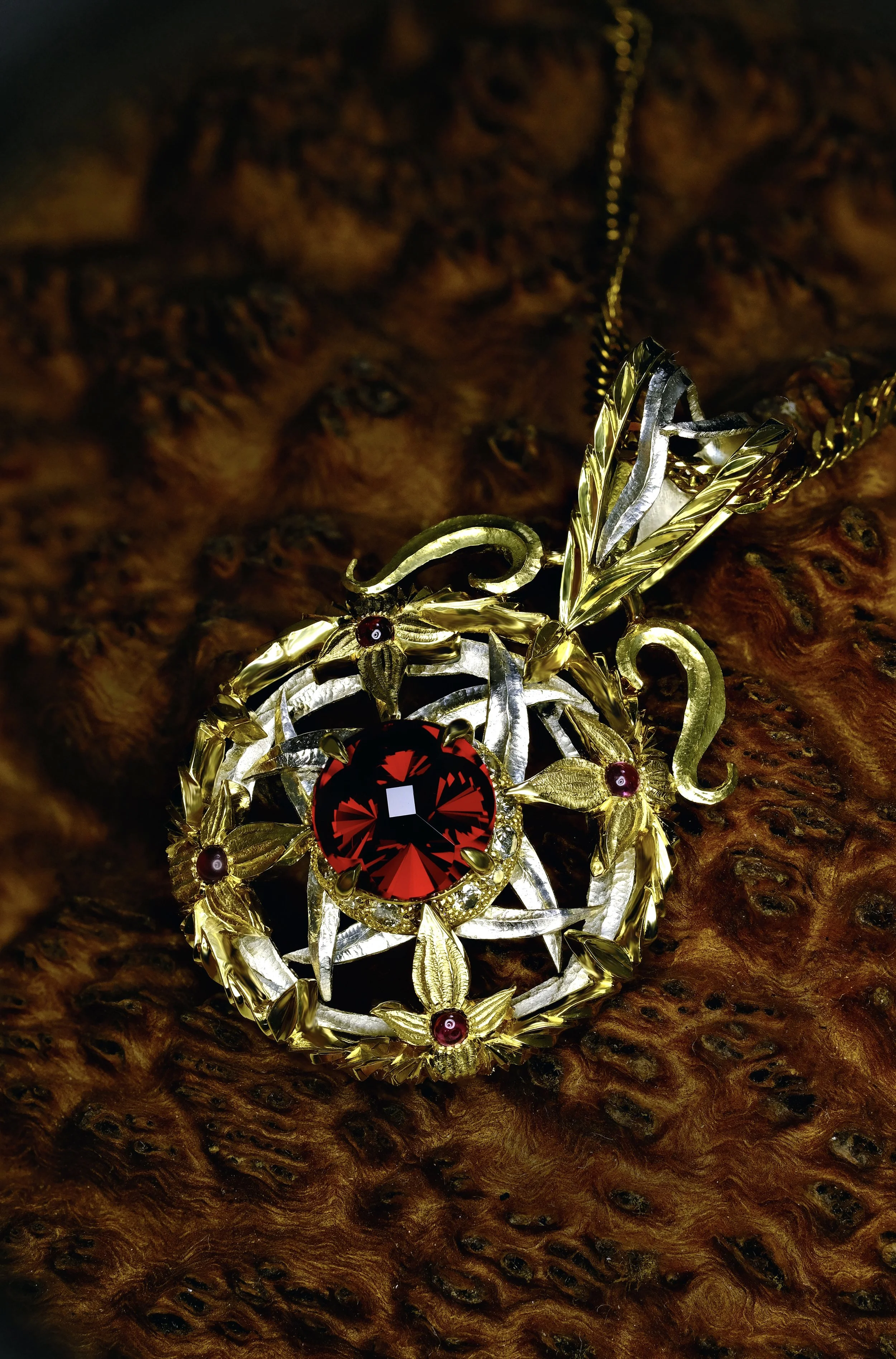 Gold and platinum handmade pendant with a round deep red garnet center, floral and leaf details, and small red accent stones, shown on a chain against textured wood background.