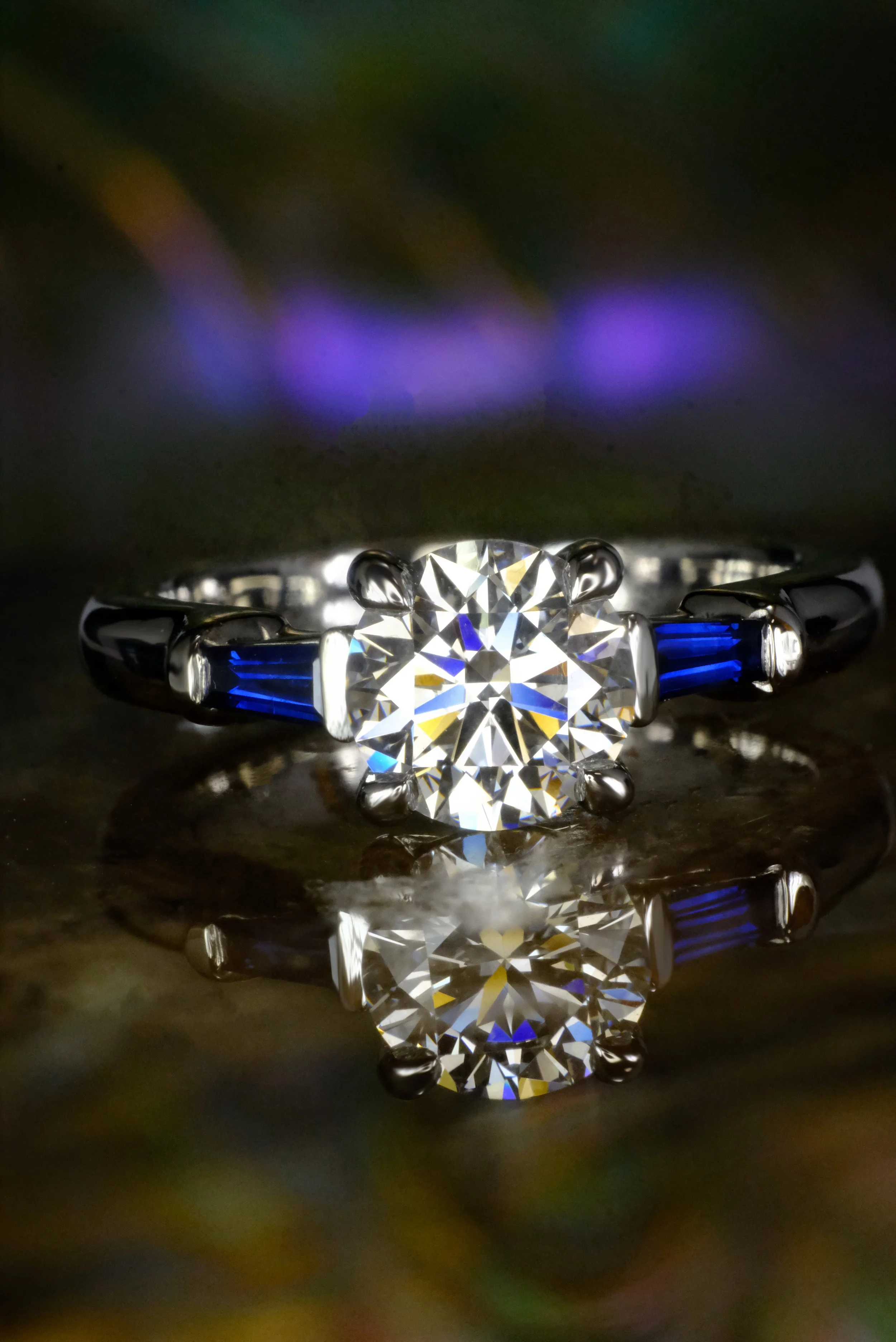 Platinum ring with a round diamond center, flanked by vivid blue baguette sapphires set into a polished band, shown from the front.