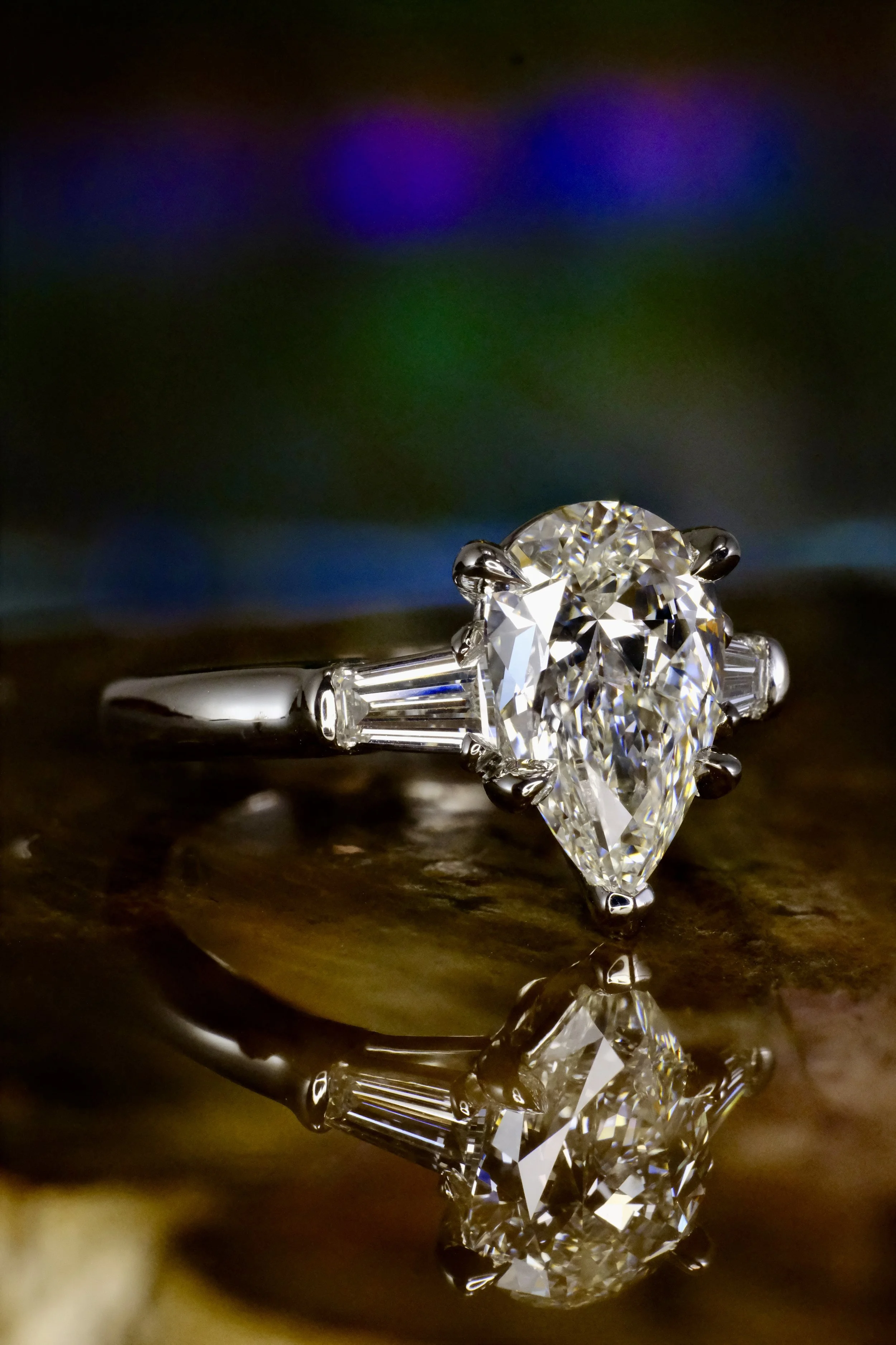 Platinum ring shown at an angle, highlighting the pear-shaped diamond and tapered baguette side stones along the band.
