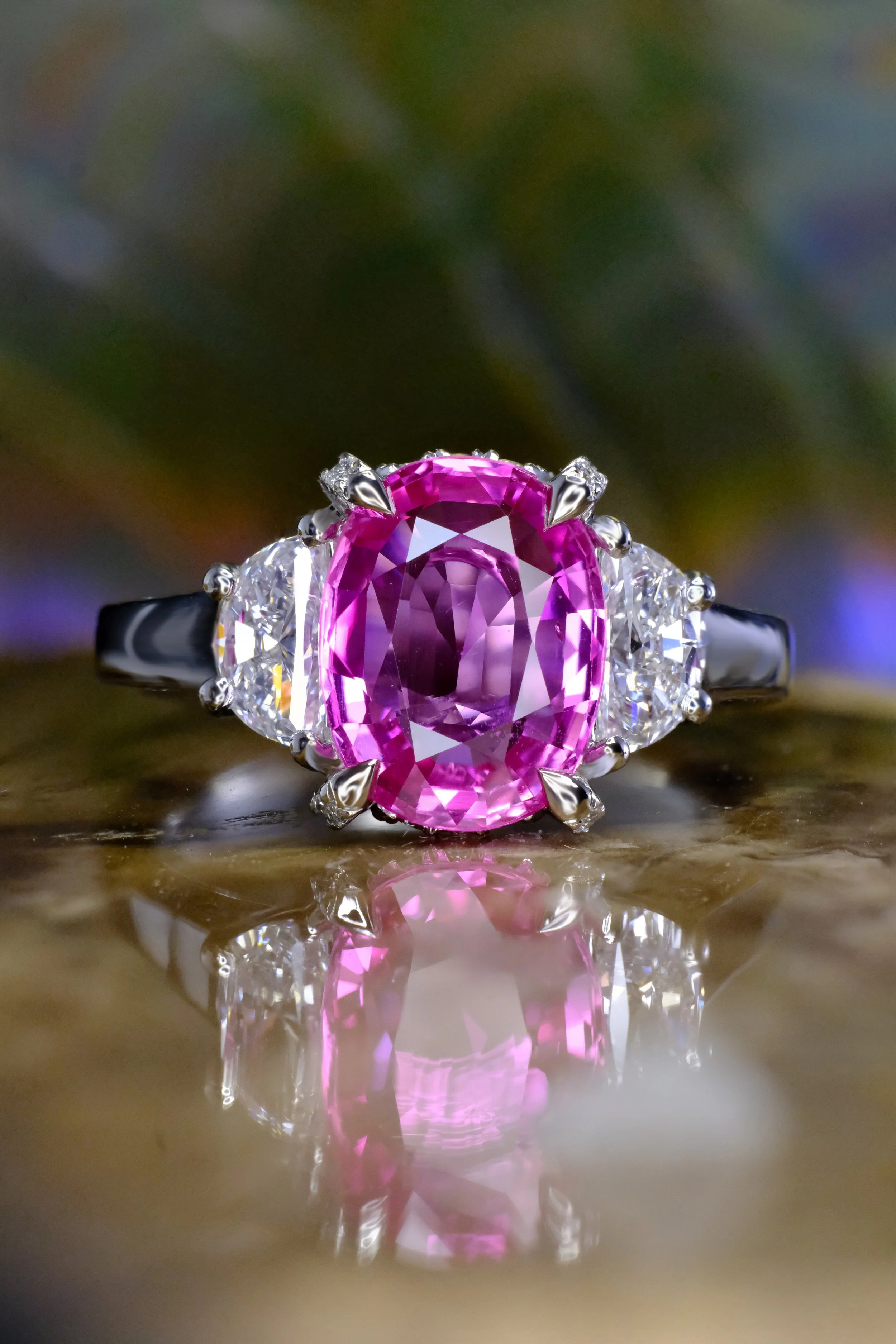 Platinum ring with oval pink gemstone and diamond side stones, shown head-on with reflection.