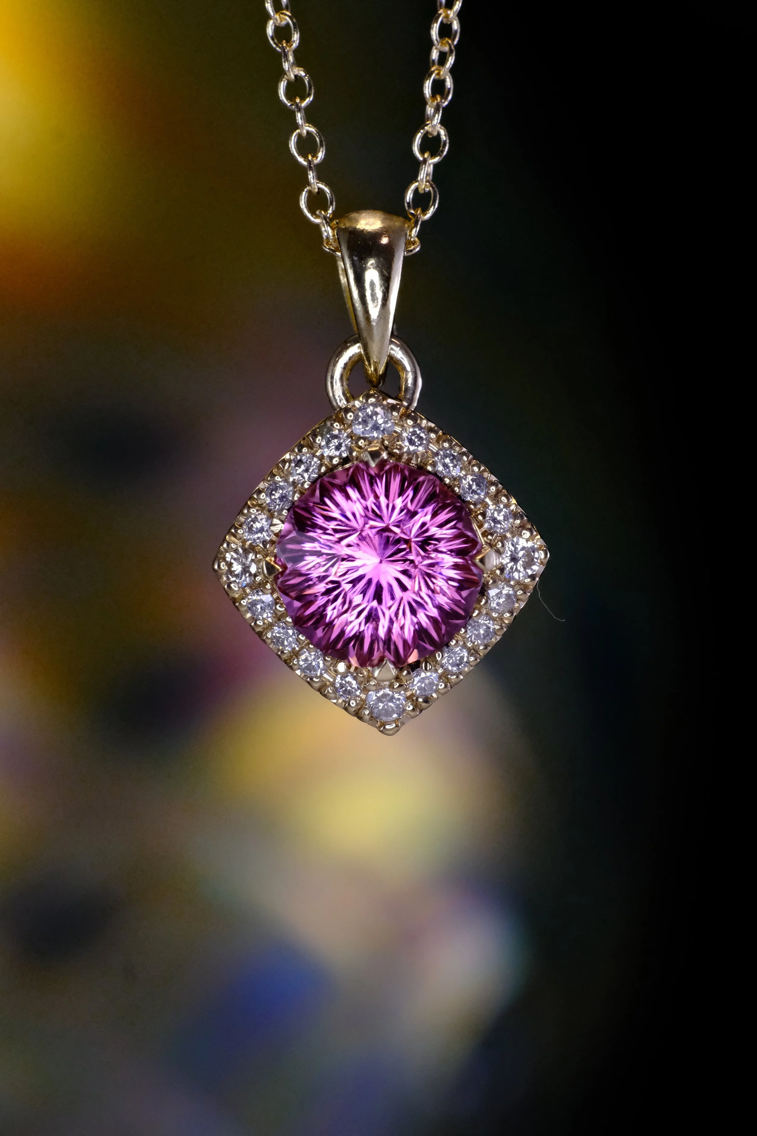 Pink-purple round gemstone pendant in yellow gold, set in a diamond halo with matching gold bail on a chain.
