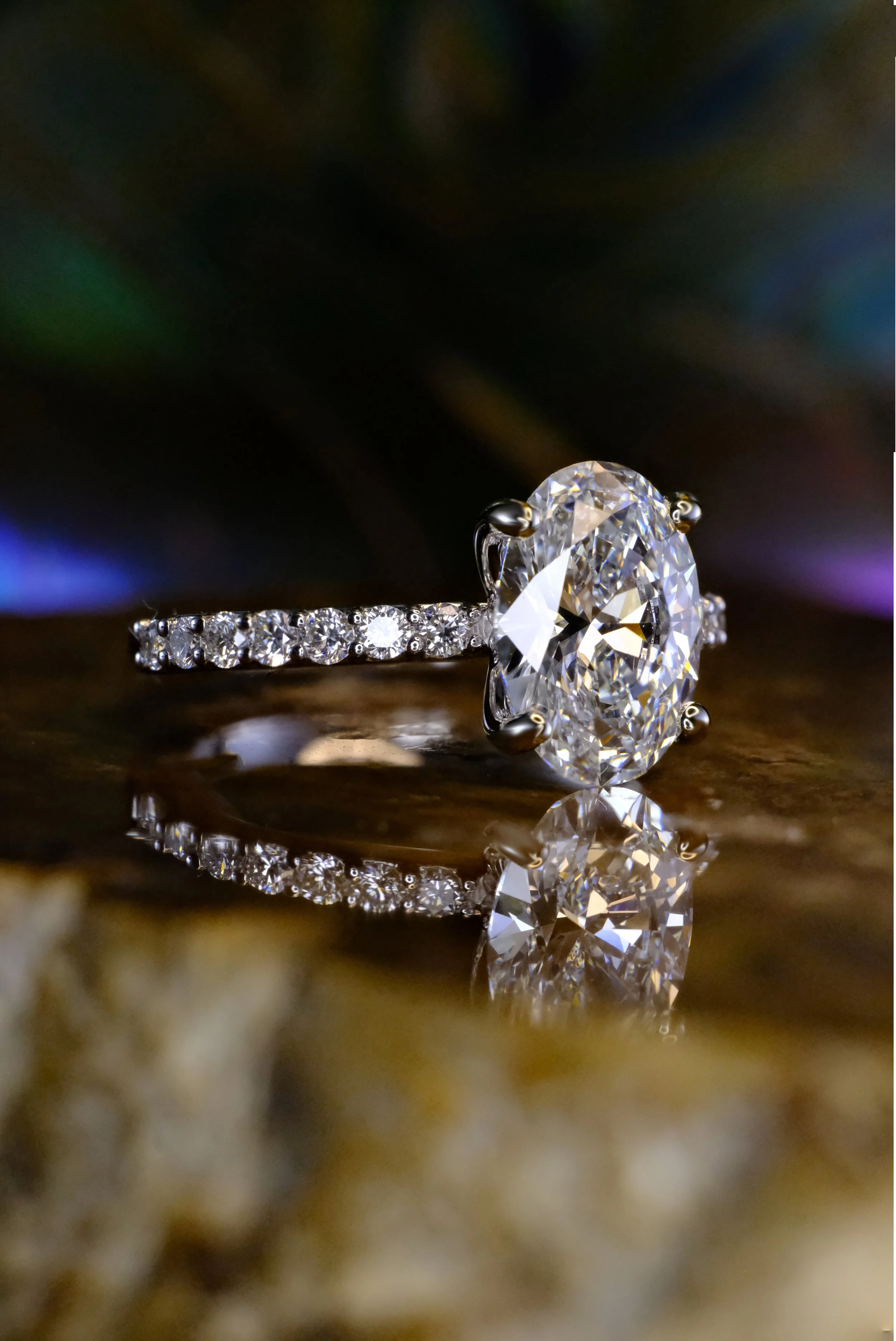 White metal ring with oval diamond and pavé band, shown from the side highlighting the setting and band detail.