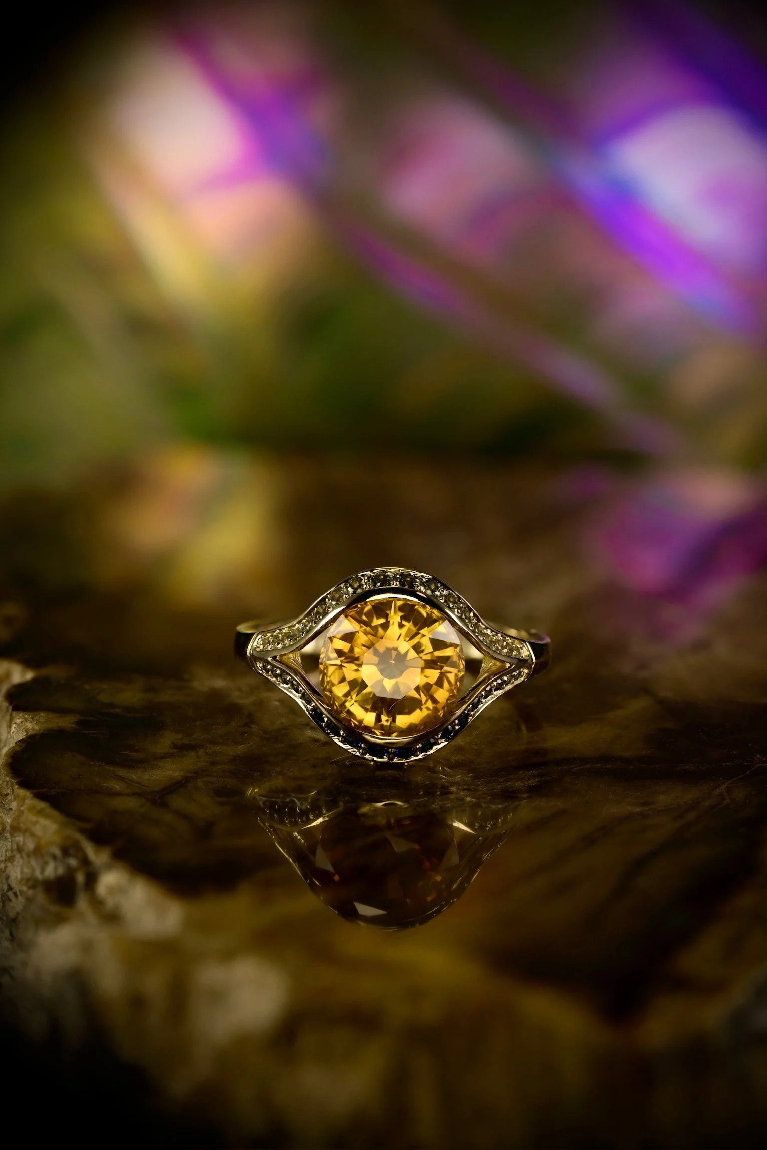 Yellow gold ring with a round orange sapphire center and curved diamond accents framing the stone.