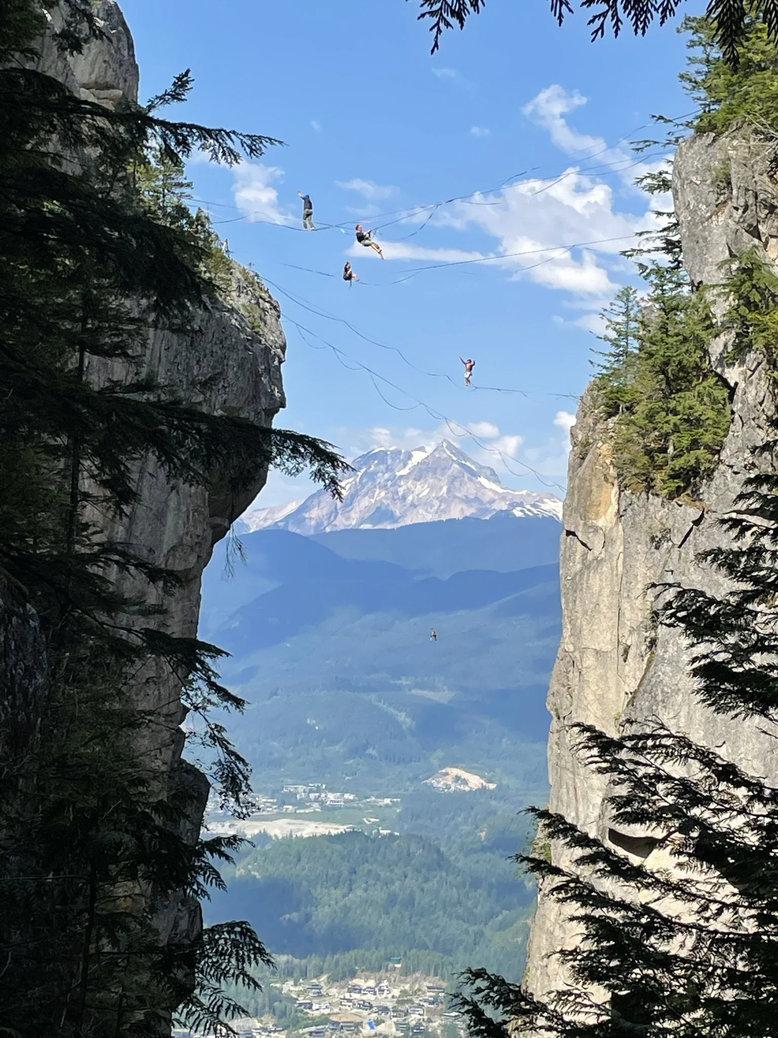 People highlining between two cliffs on the Chief and Squamish, BC in the background.