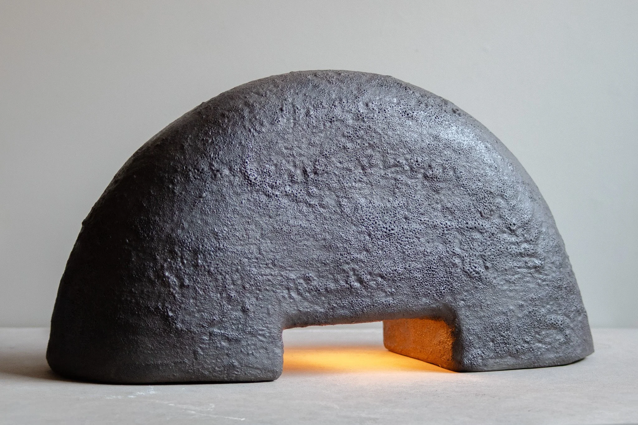 Close-up of a volcanic rock sculpture with a small section lit from below, depicting a rounded, textured surface and an orange foreground element.