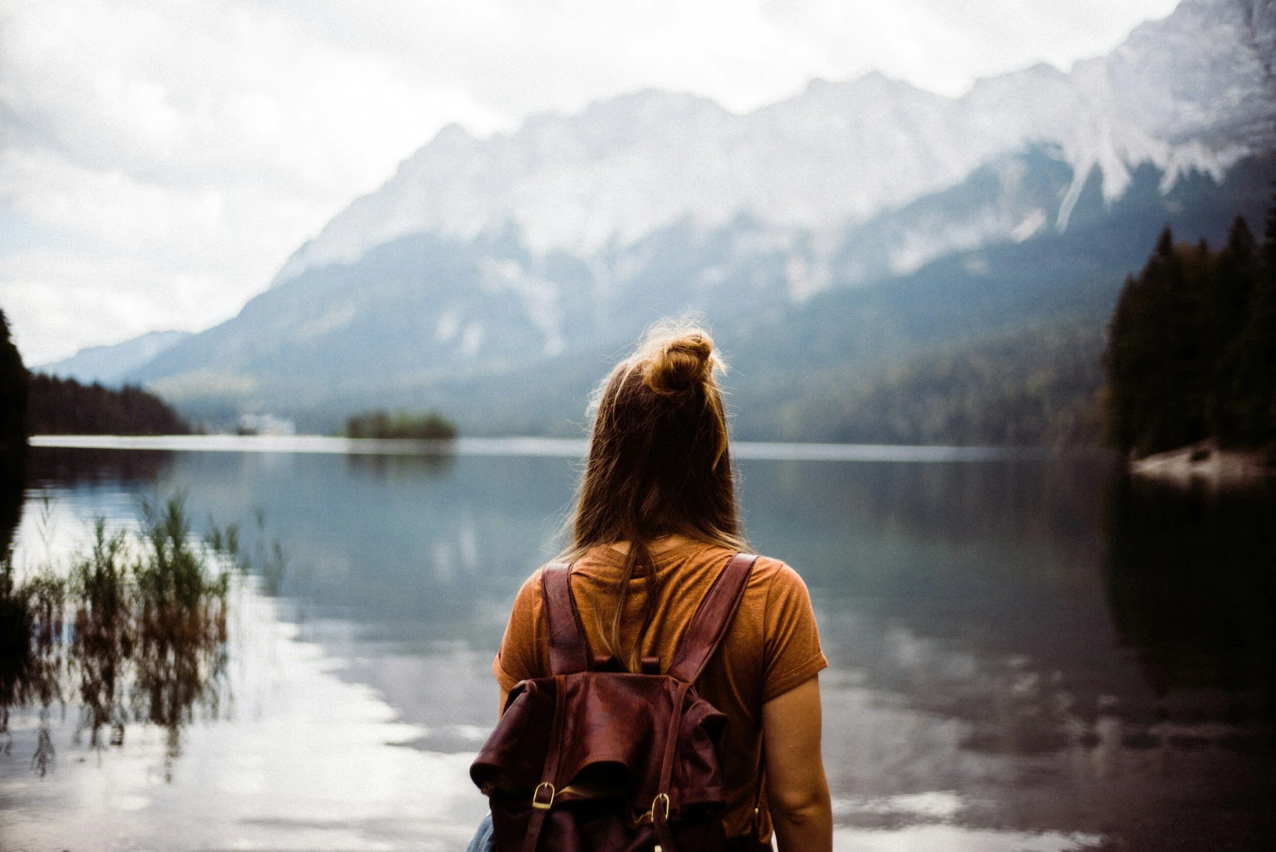 Woman with a backpack looking out at a lake and mountain range.