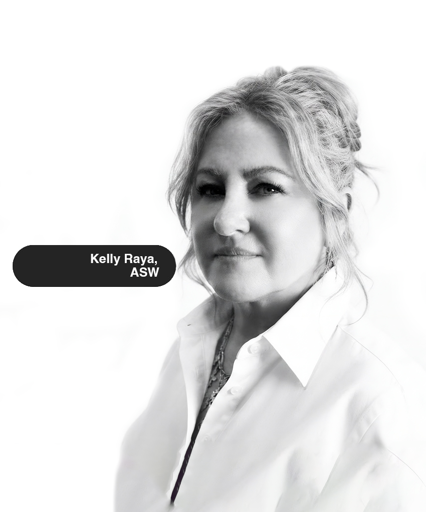 Black and white portrait of Kelly Raya, a woman with shoulder-length wavy hair, wearing a white collared shirt, layered necklaces, and a blazer, against a plain background. Victoria Community Counseling, LCSWC - Riverside, CA 