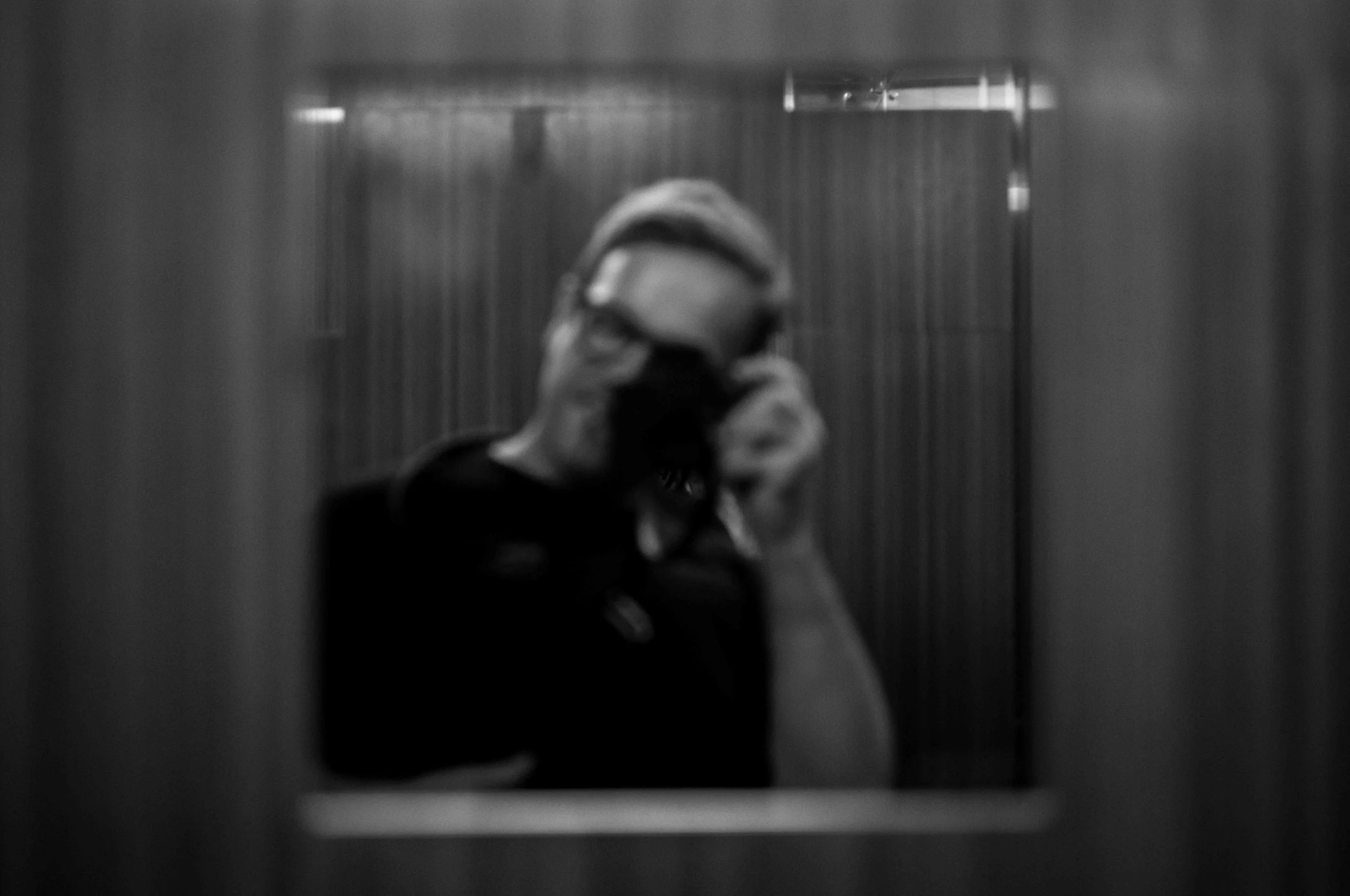 Black and white photo of a person taking a selfie in an elevator mirror, wearing a mask, with the reflection visible.