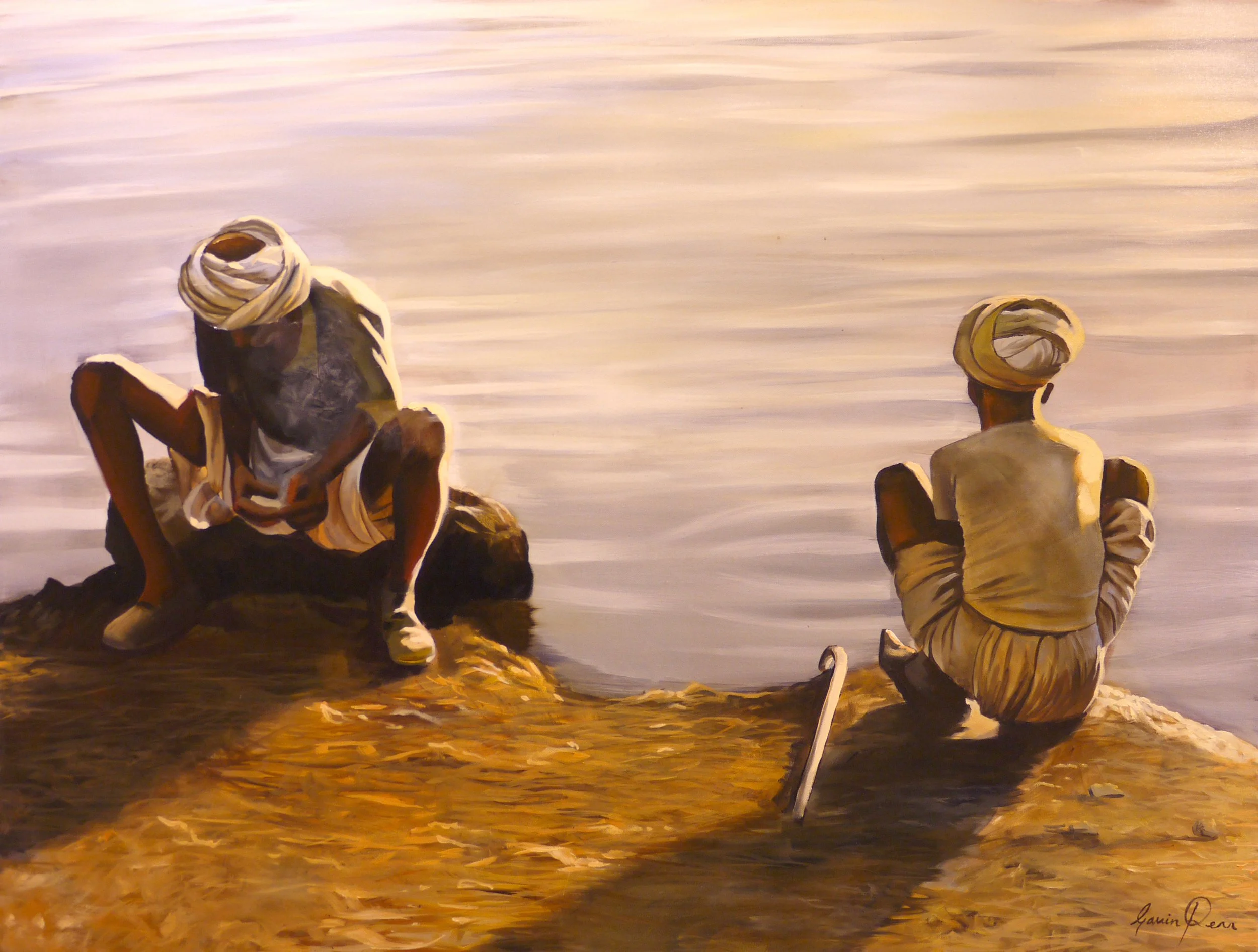 Two men wearing traditional Middle Eastern attire sitting on the beach near the water, with one man sitting on a rock and the other seated directly on the ground.