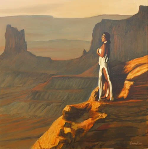 A woman in a long white dress standing on a rocky ledge overlooking a canyon at sunset.