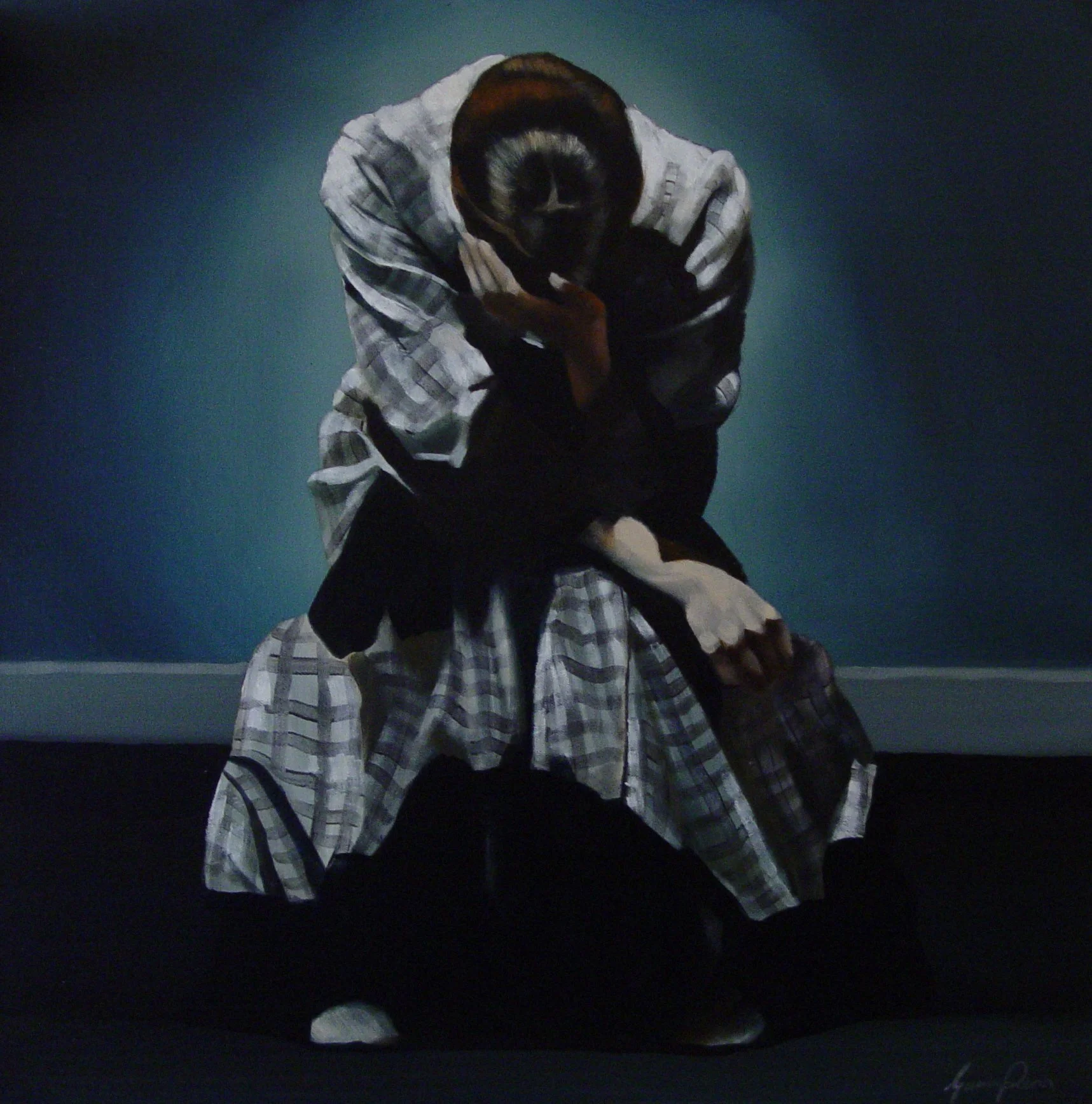 A person in a plaid shirt and dark pants is seated on the ground with their head bowed down and hand covering their face. The background is dark and greenish.