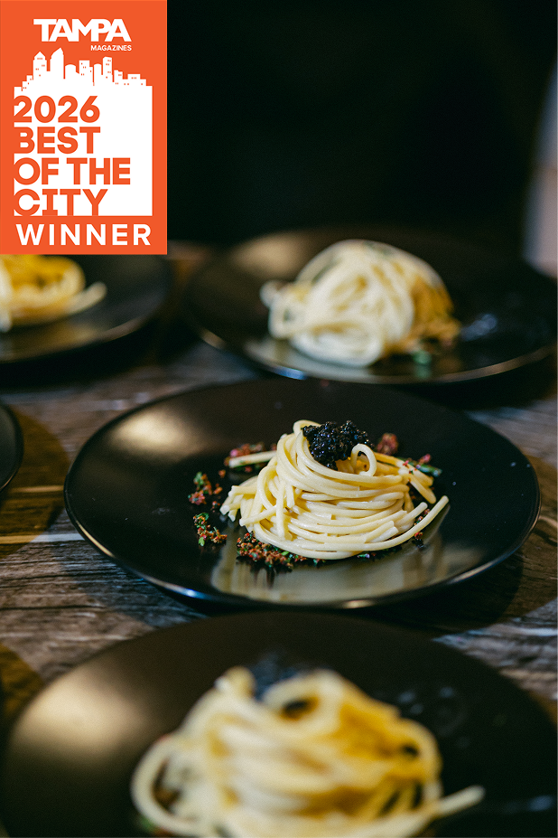 Tampa Magazine 2026 Best of the City Winner badge overlaid on a close-up photo of plated pasta with caviar on a black plate, with additional plates visible in the background on a wooden table.