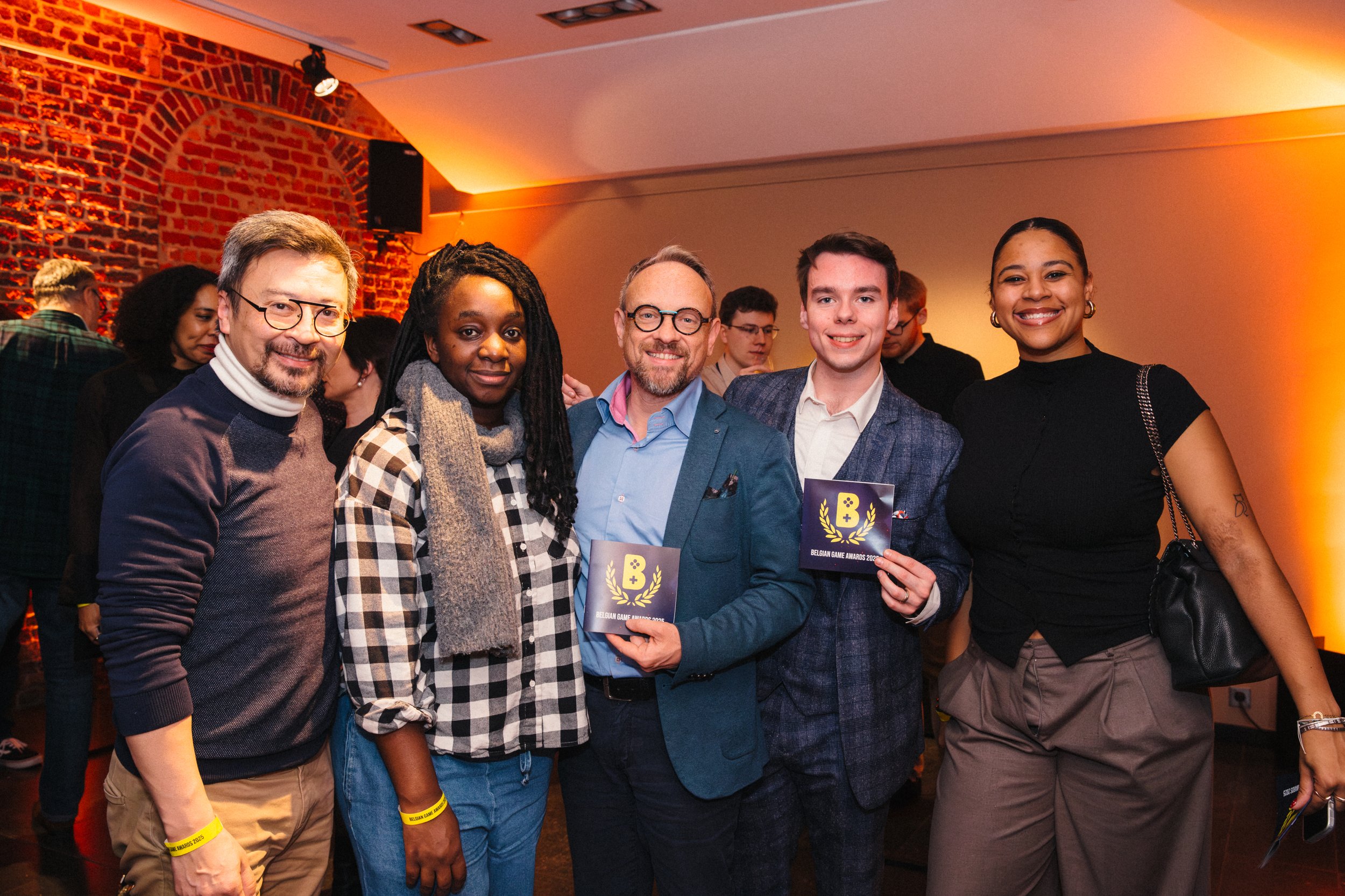 Five people smiling and holding awards at an indoor event with brick walls and warm lighting.