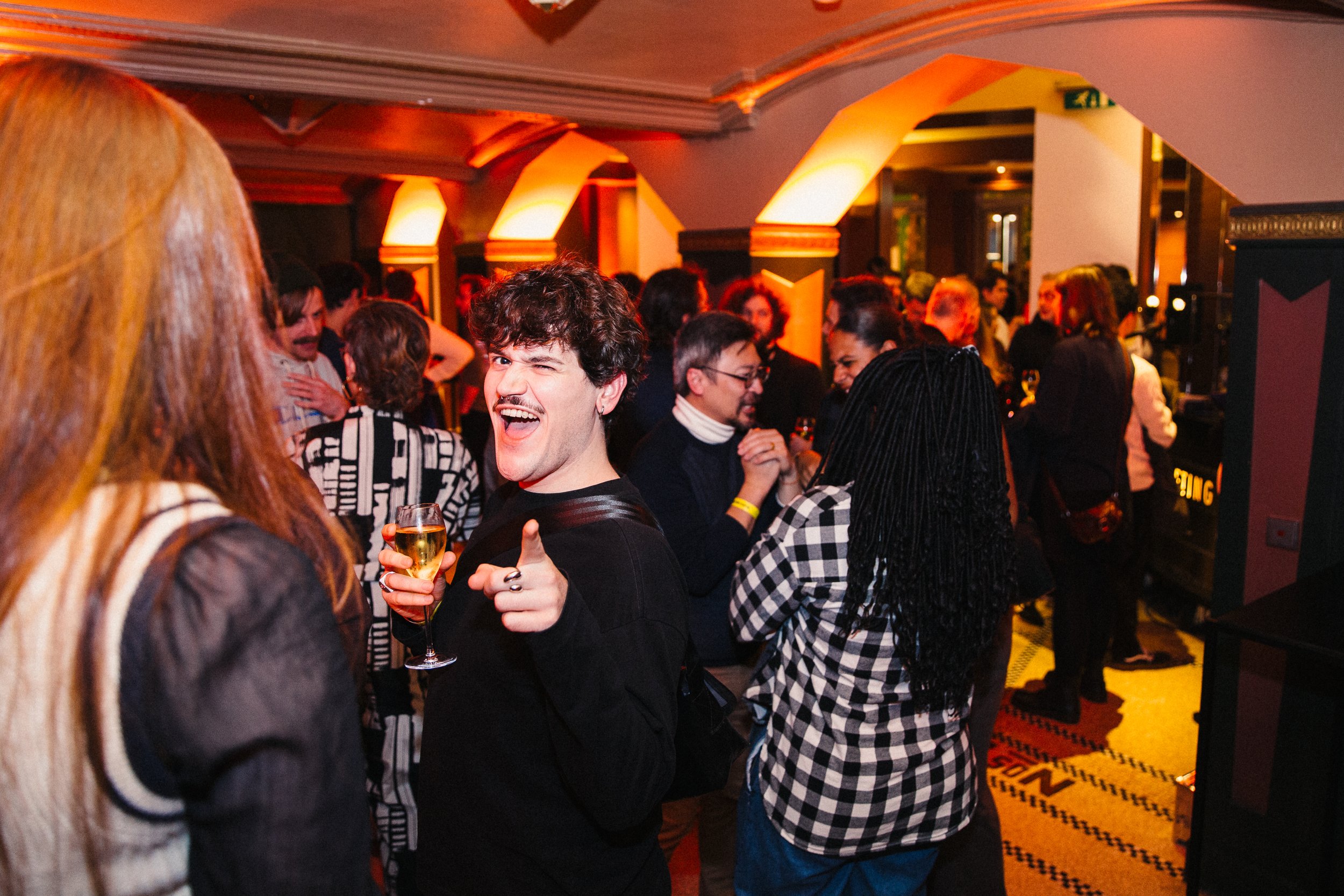 A lively social gathering at a bar or nightclub with people holding drinks, engaging in conversation and enjoying the lively atmosphere with warm lighting and stylish decor.