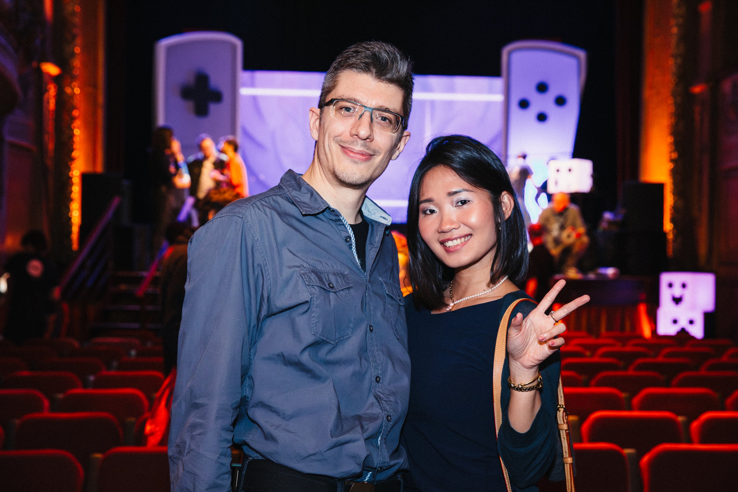 A man and woman smiling and posing together inside a theater with a stage in the background, during a live performance or event.