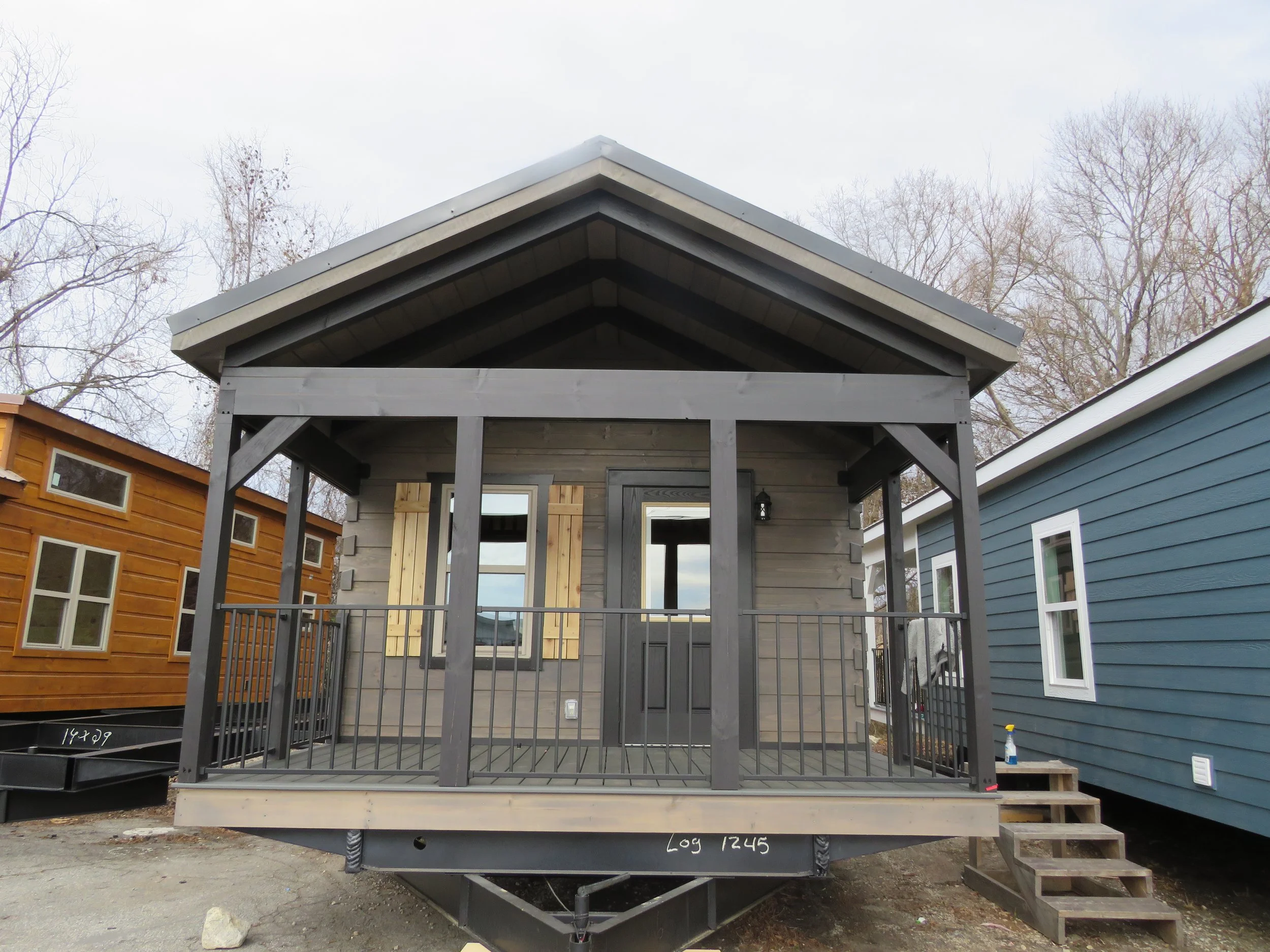 Small gray wooden house with open front porch and wooden stairs, surrounded by other houses.
