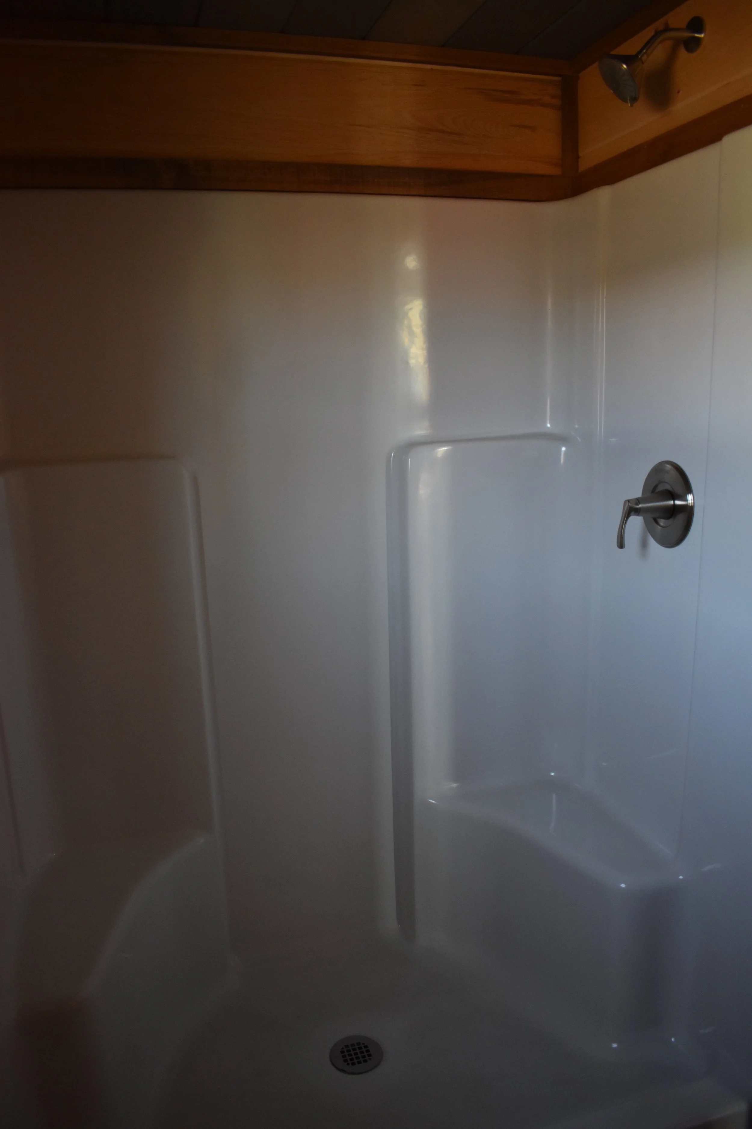 Empty shower stall with a handheld showerhead on the upper right, a single control handle, and a built-in seat on the lower left, with a drain at the bottom.