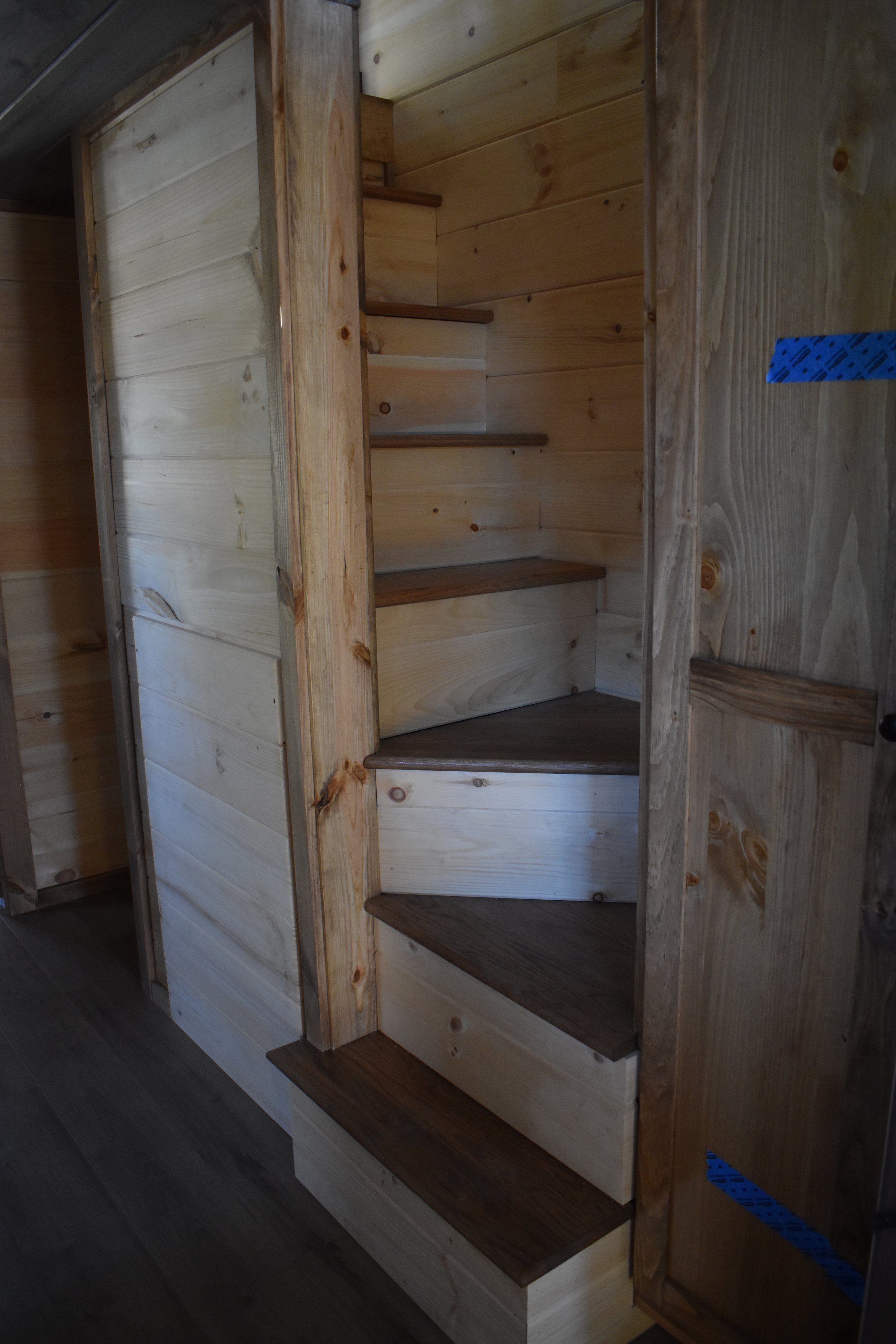 Interior of a wooden staircase with dark and light wood steps, surrounded by unfinished wood walls.