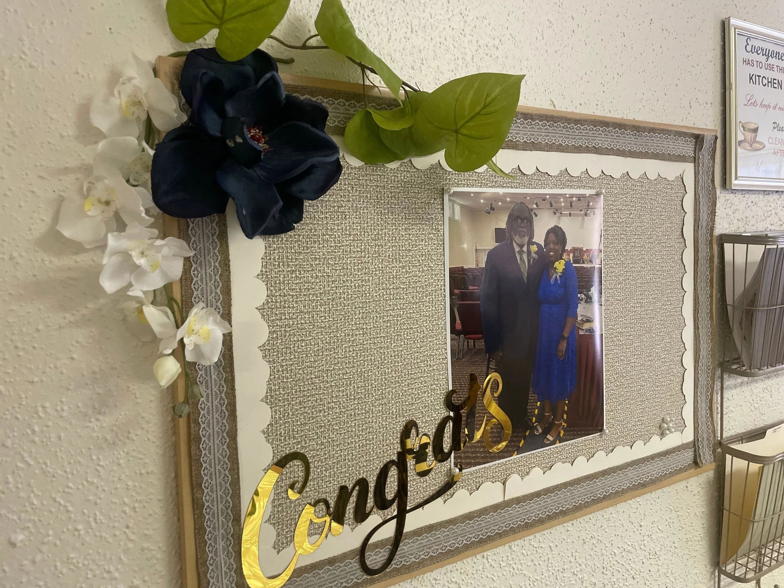 Decorative congratulations bulletin board with a framed photo of a man and woman, floral accents, and a 'Congrats' sign.