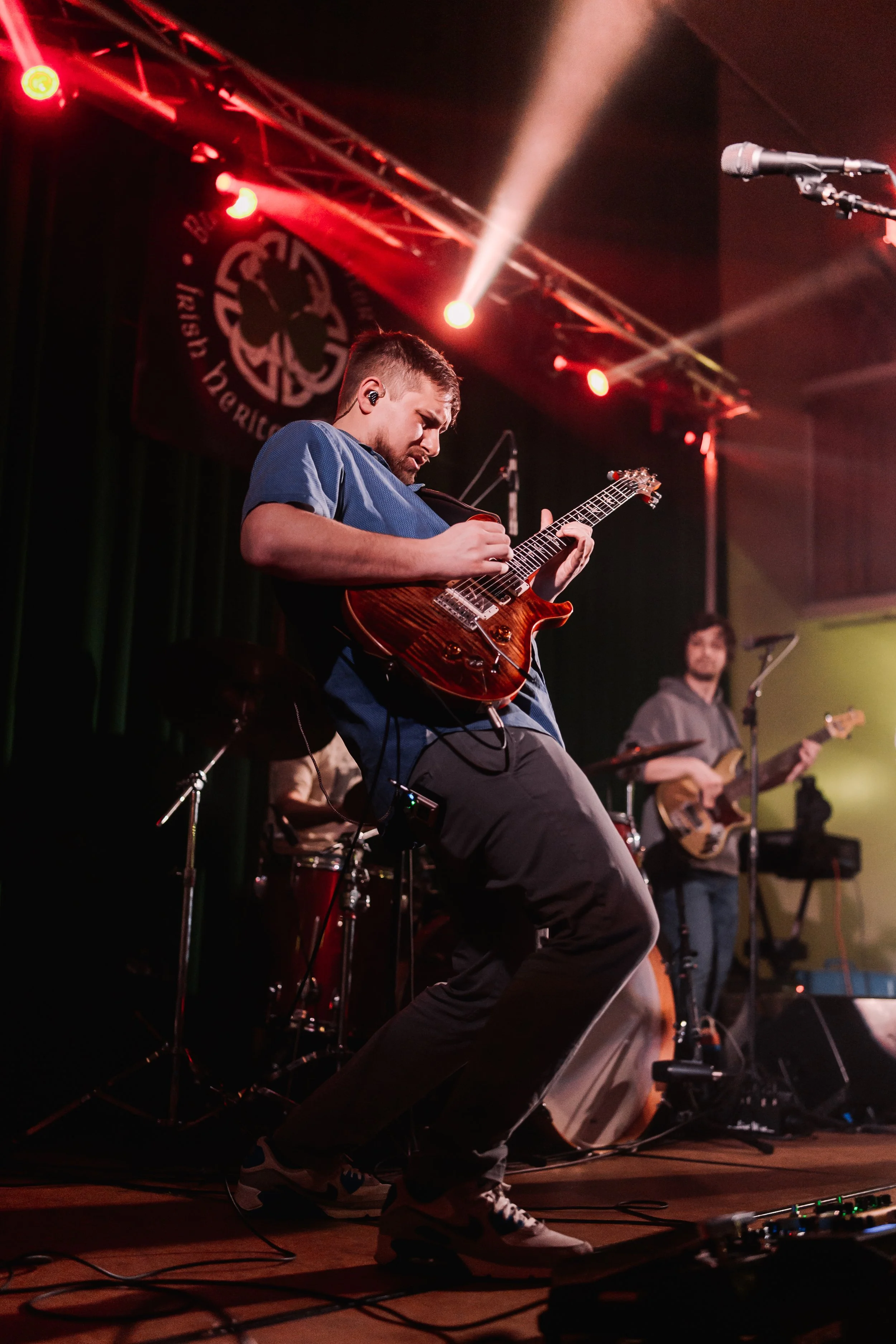 A man playing an electric guitar on stage with green and blue stage lights in the background.