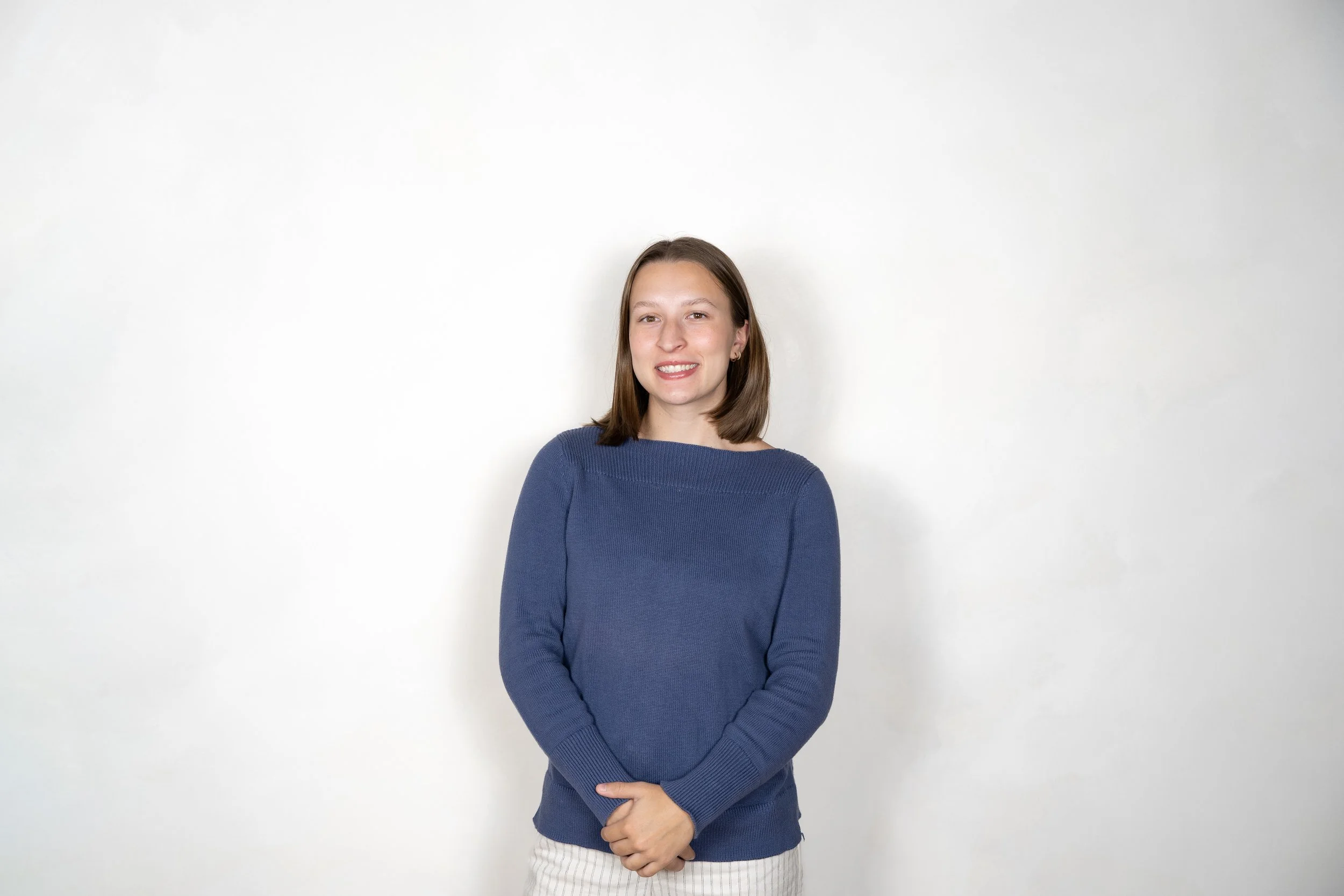 A young man with a smile, wearing a black cap with a white lion logo, a gray hoodie with black text on the sleeve, standing against a plain white background.
