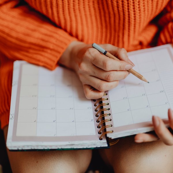 woman wearing orange sweater holding pencil and writing in agenda book