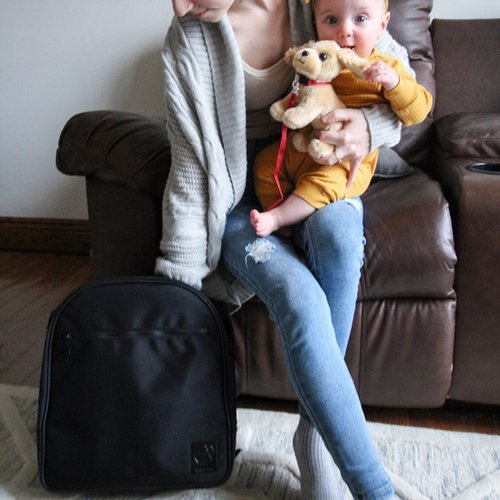 mom holding smiling baby while reaching into diaper bag back pack