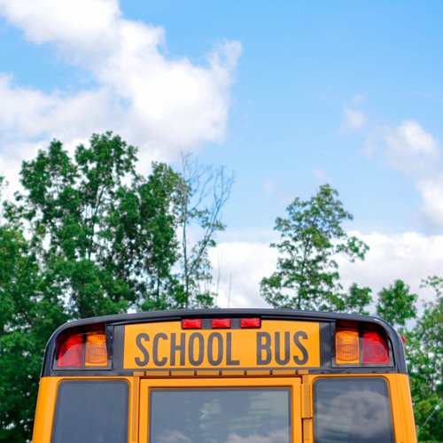 back of school bus in driving away; green trees and blue skies in the background