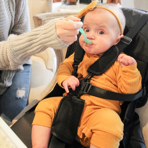 baby sitting in high chair being fed by mom