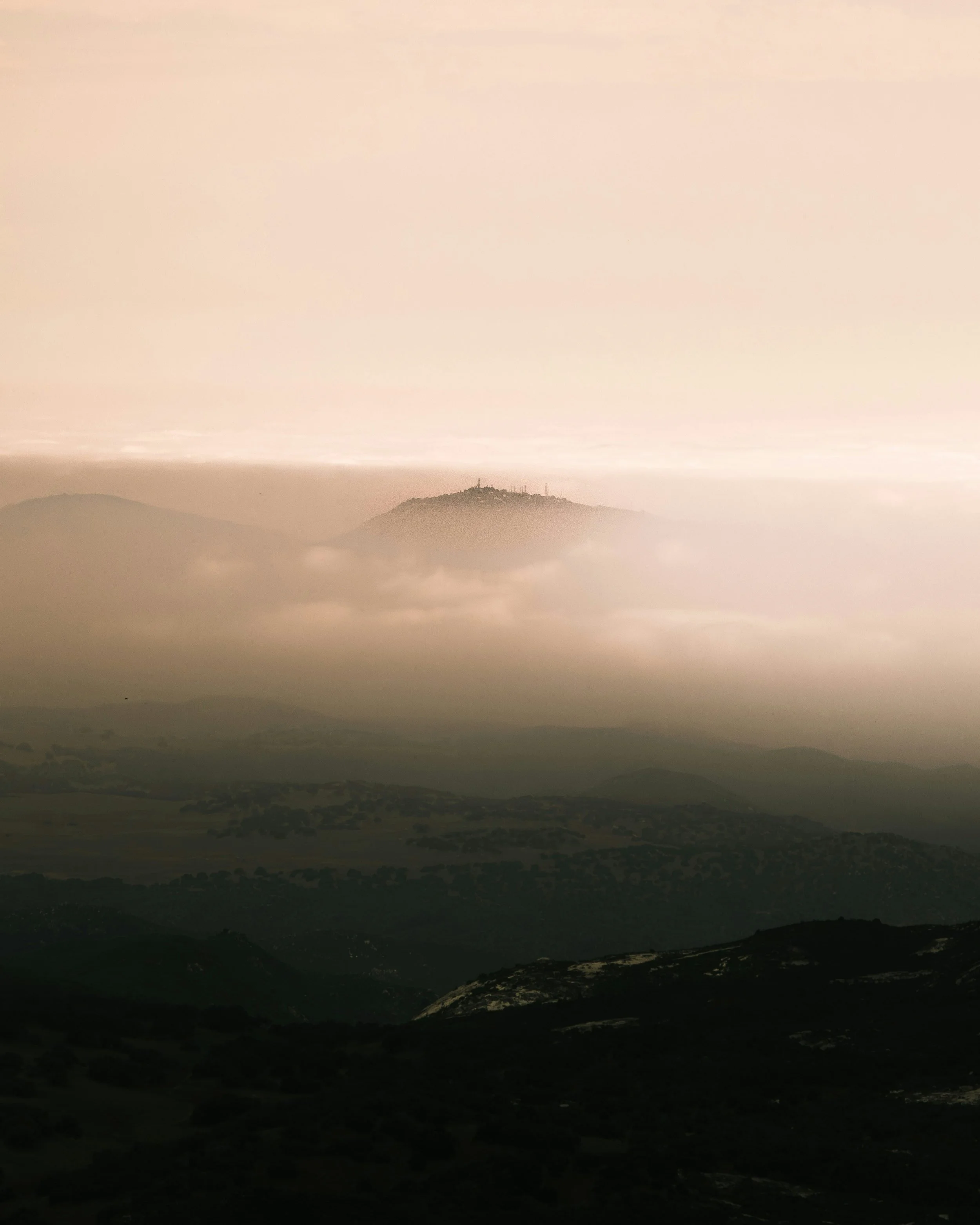 Mount Woodson rises out of the clouds in San Diego County at sunrise. Much of the land around it can barely be seen, but the top of the hill is catching the soft light