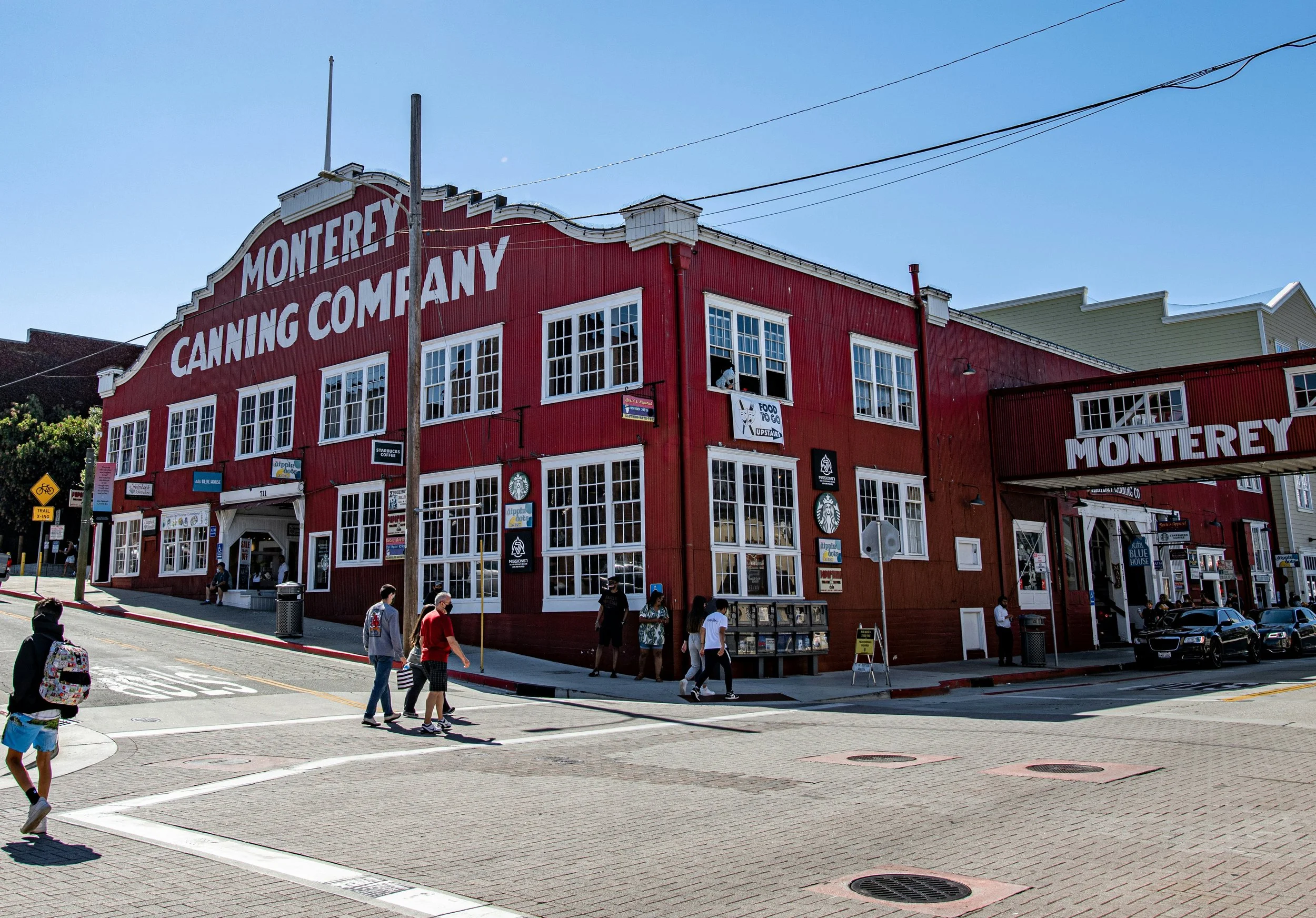 People walk past a huge red building with the word: Moterey Canning Company, written in white. Drives & Detours Monterey Tour