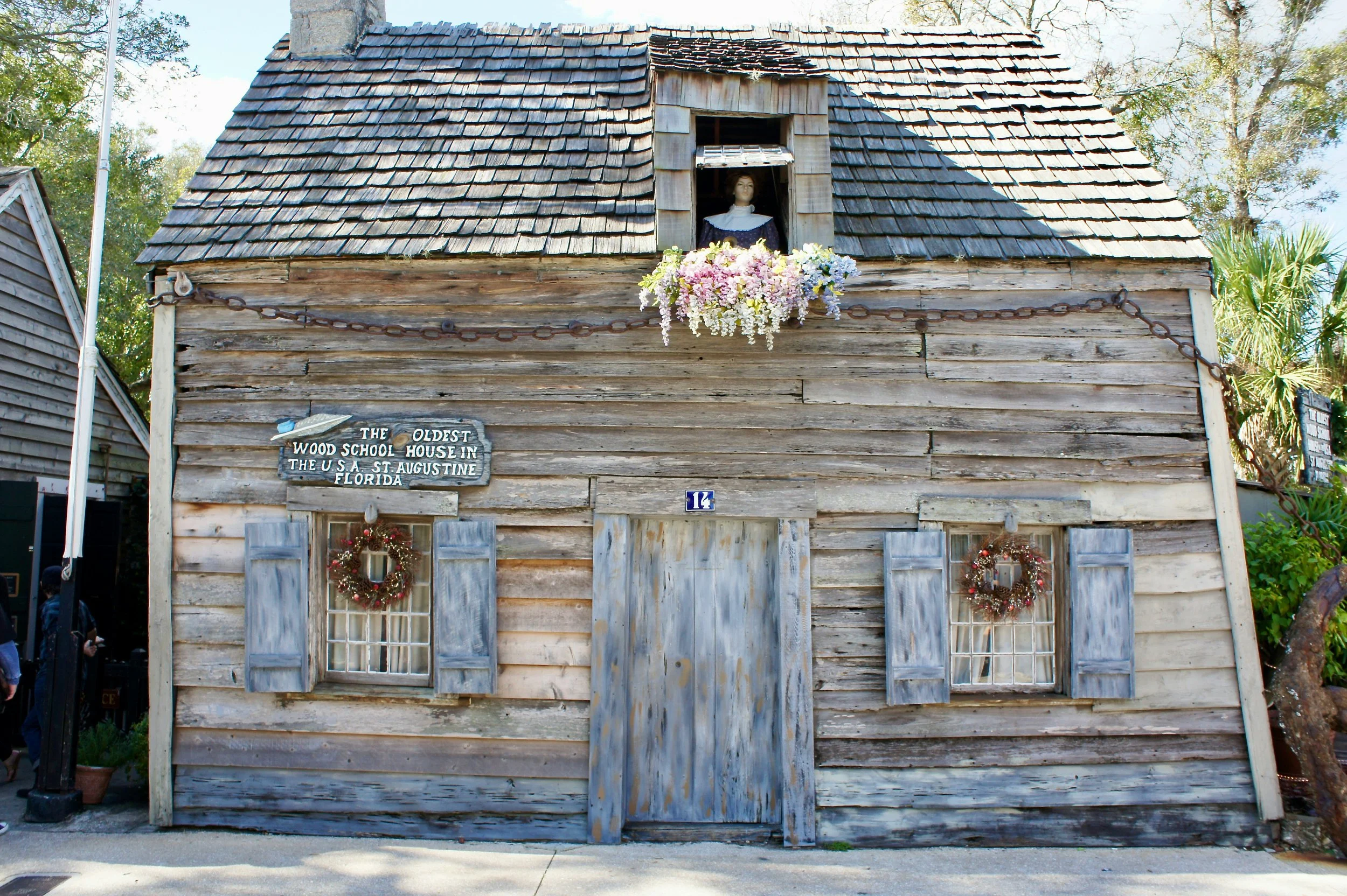 The Oldest Wooden School House Historic Museum & Gardens in St. Augustine is a tumbledown wooden hut. Flowers hang from the windows