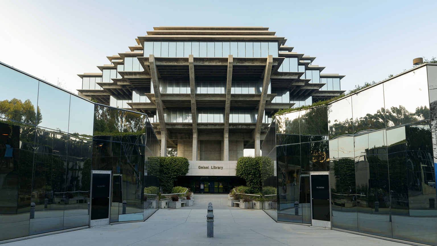 The Geisel Library at UC San Diego from the front. Mirrored glass reflects the three tiers that can be seen, which are reflecting the sky in the glass