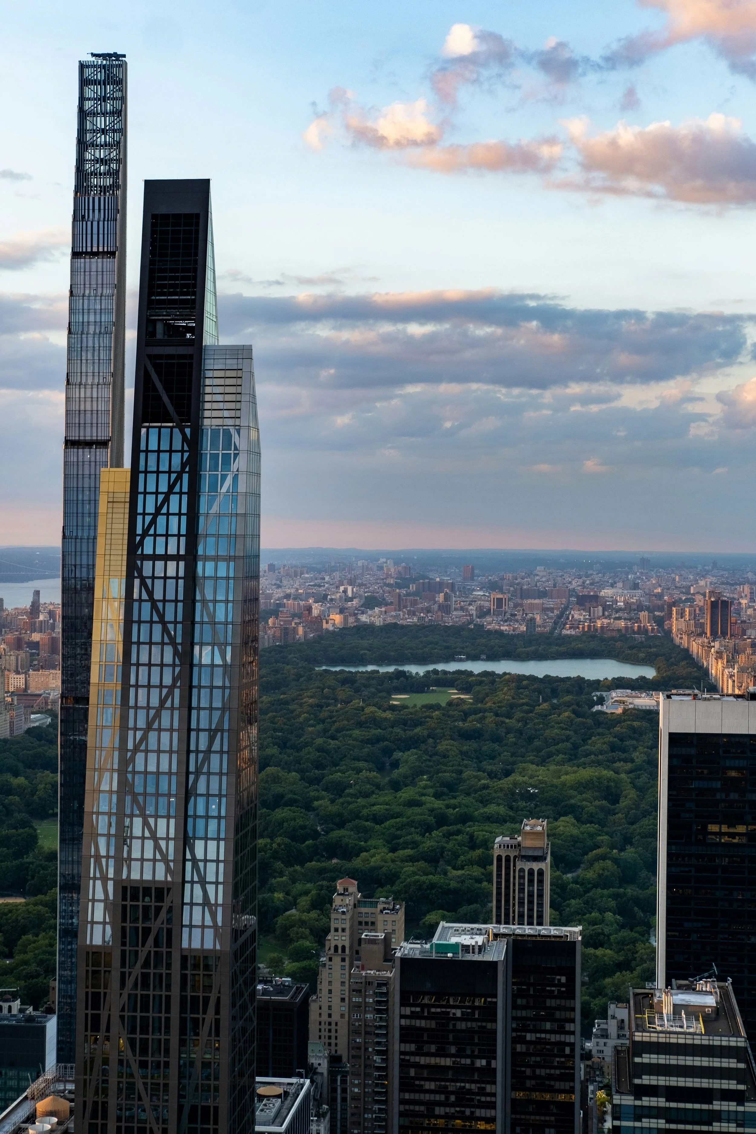 A skyscraper frames an aerial view of Central Park, New York. The park stretches into the distance, lined by other skyscrapers