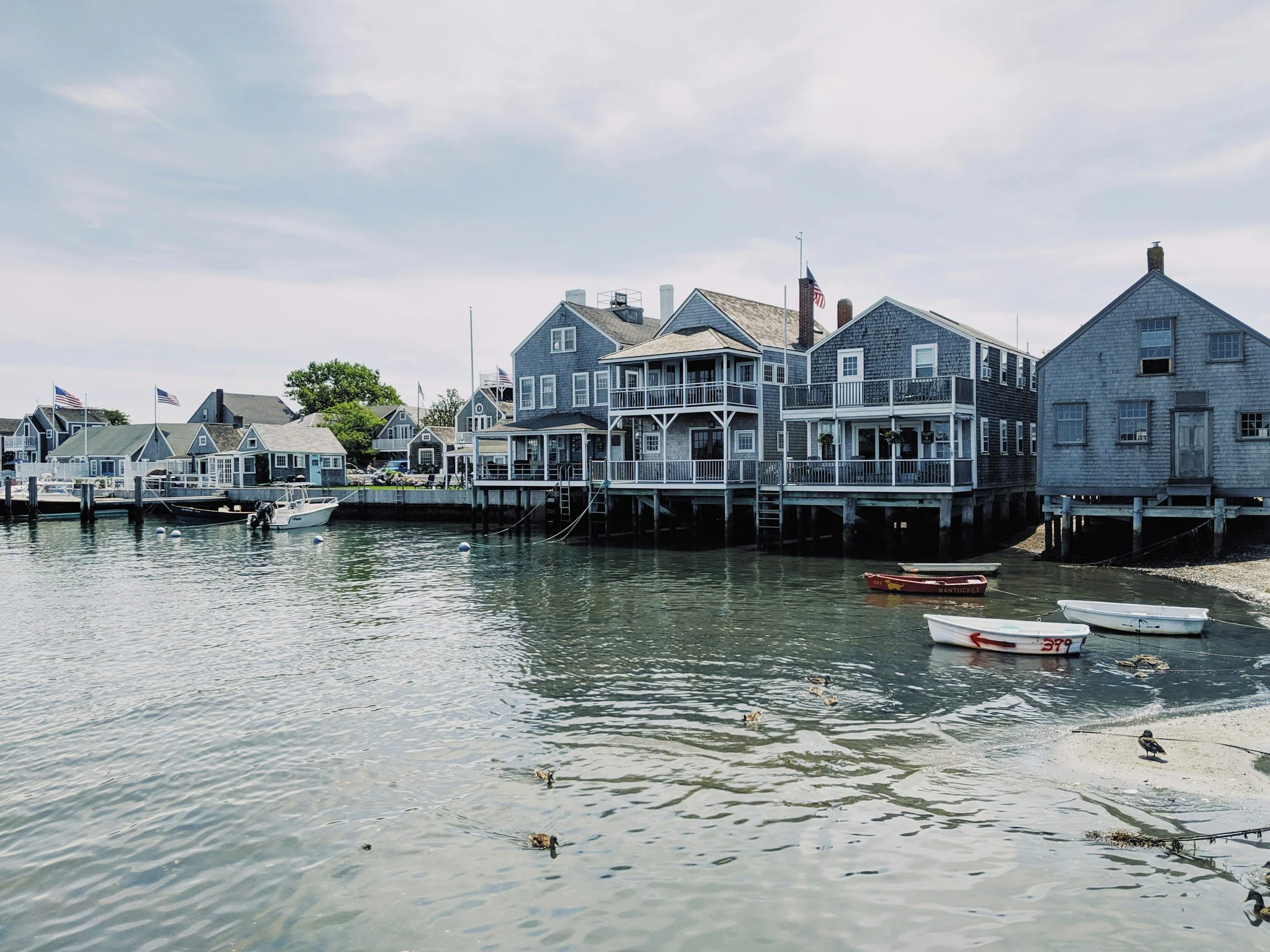 Wooden houses and docks line the shore in Nantucket Town. A few dinghies bob in the still water