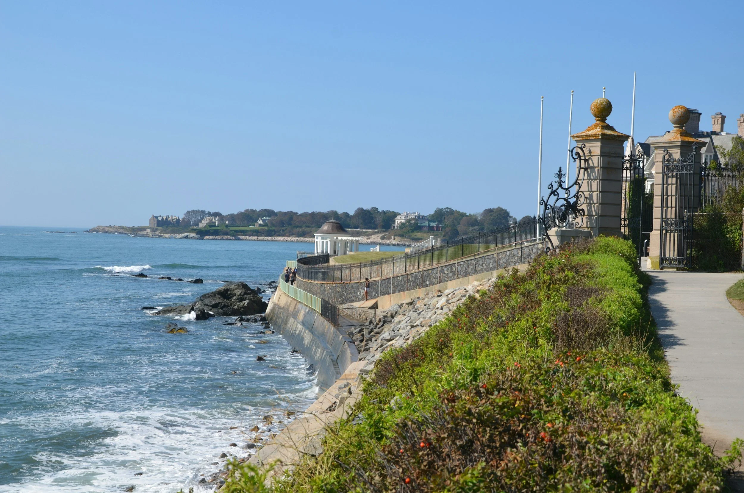 Newport Cliff Walk runs through a large set of iron gates to the sea with Mansions in the distance on a headland