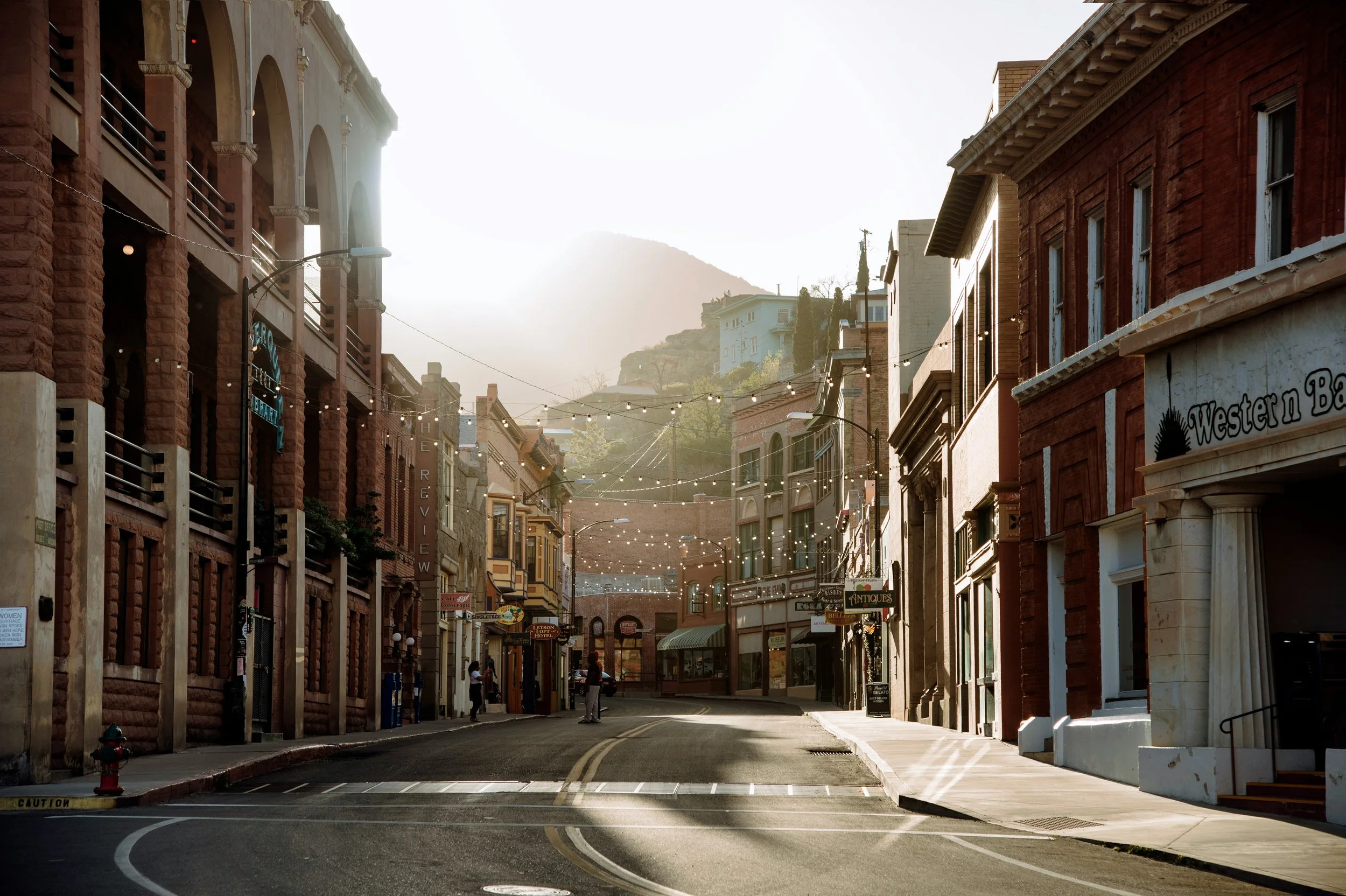 The sun shines through an old street lined with red brick buildings in Arizona. Drives & Detours Bisbee Tour