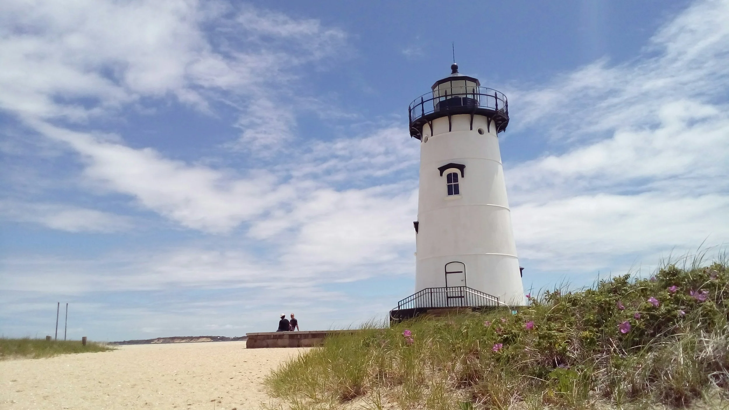 Two people sit on the sand under the small white Edgartown Lighthouse near Oak Bluffs. Drives & Detours Top sights in Martha's Vineyard