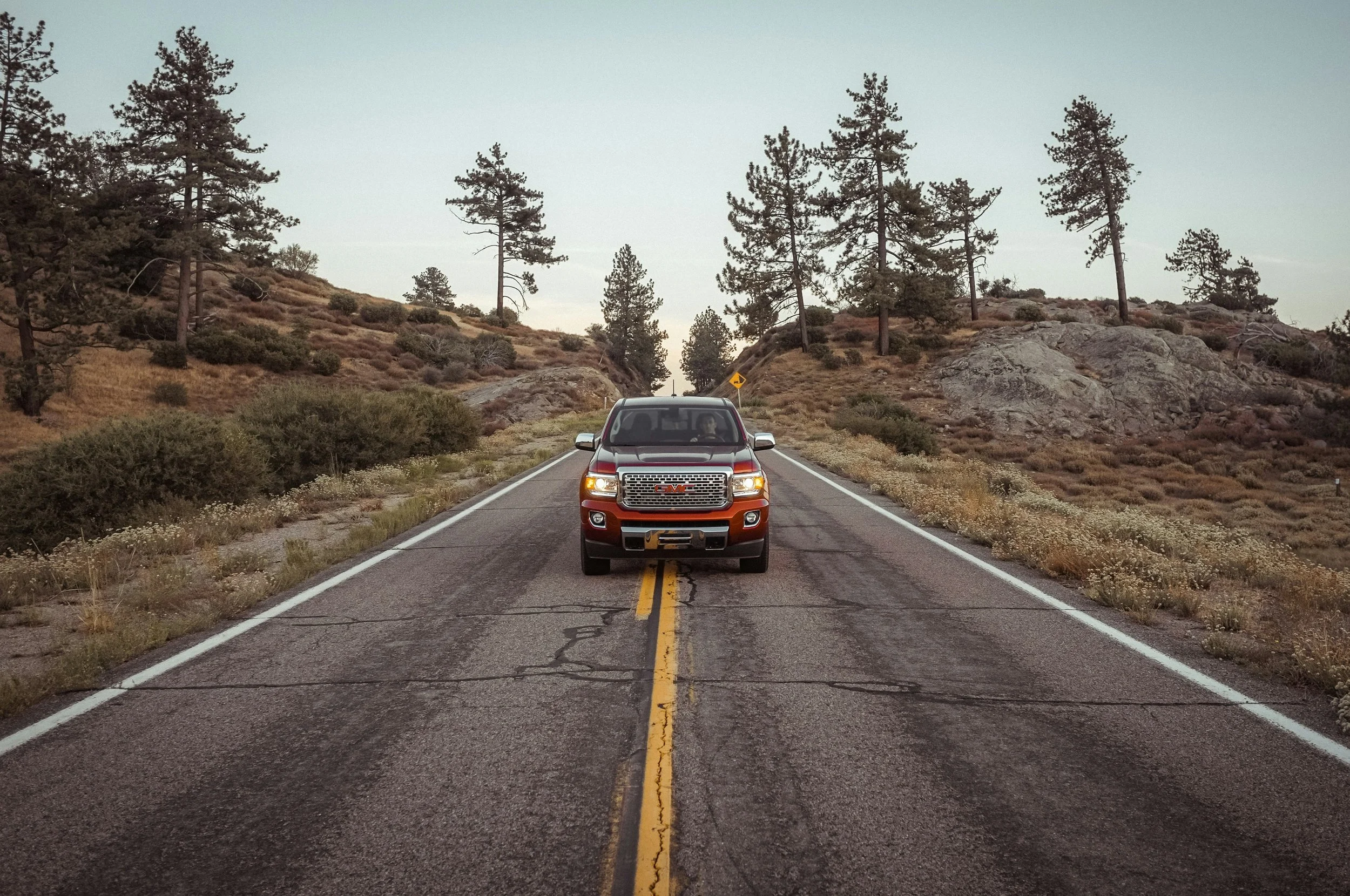 A pickup truck drives along a narrow road in San Diego County. Trees and shrub line both sides of the road