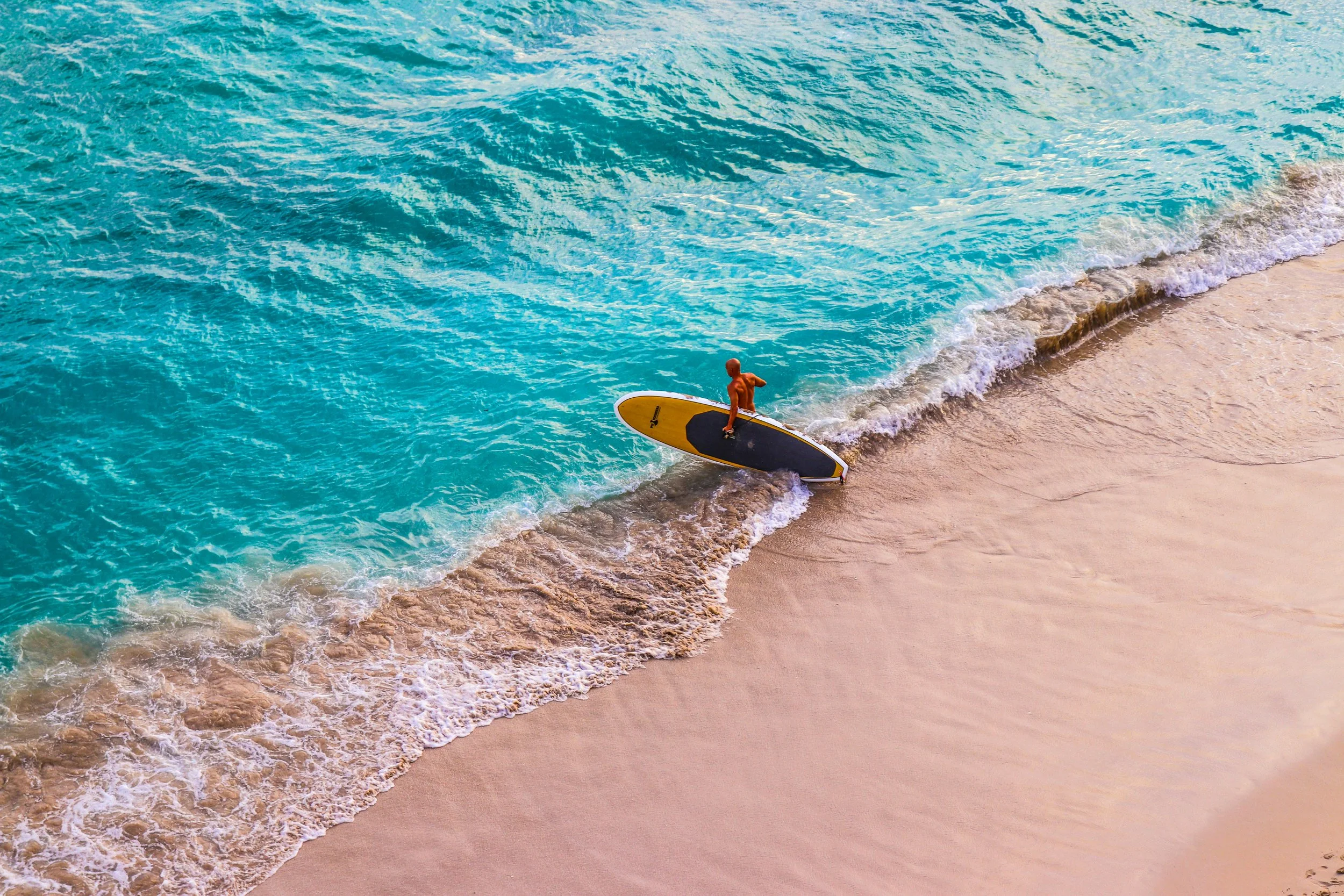 A man carrying a surfboard plunges into the water from the beach in Honolulu. Drives & Detours Waikīkī walking tour