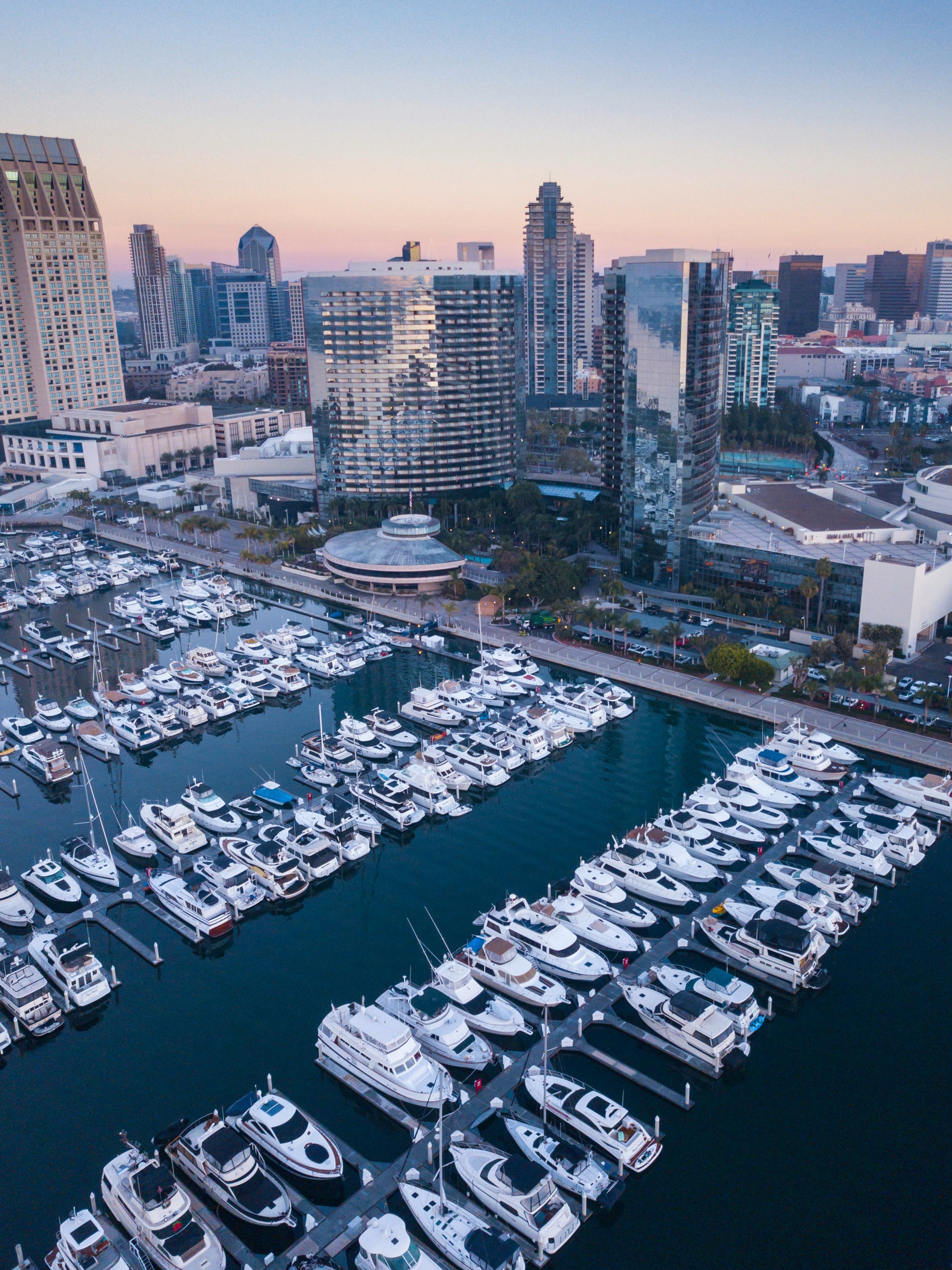Skyscrapers rise over the marina at San Diego Embarcadero. It's an aerial shot at dusk, with sky a faint orange