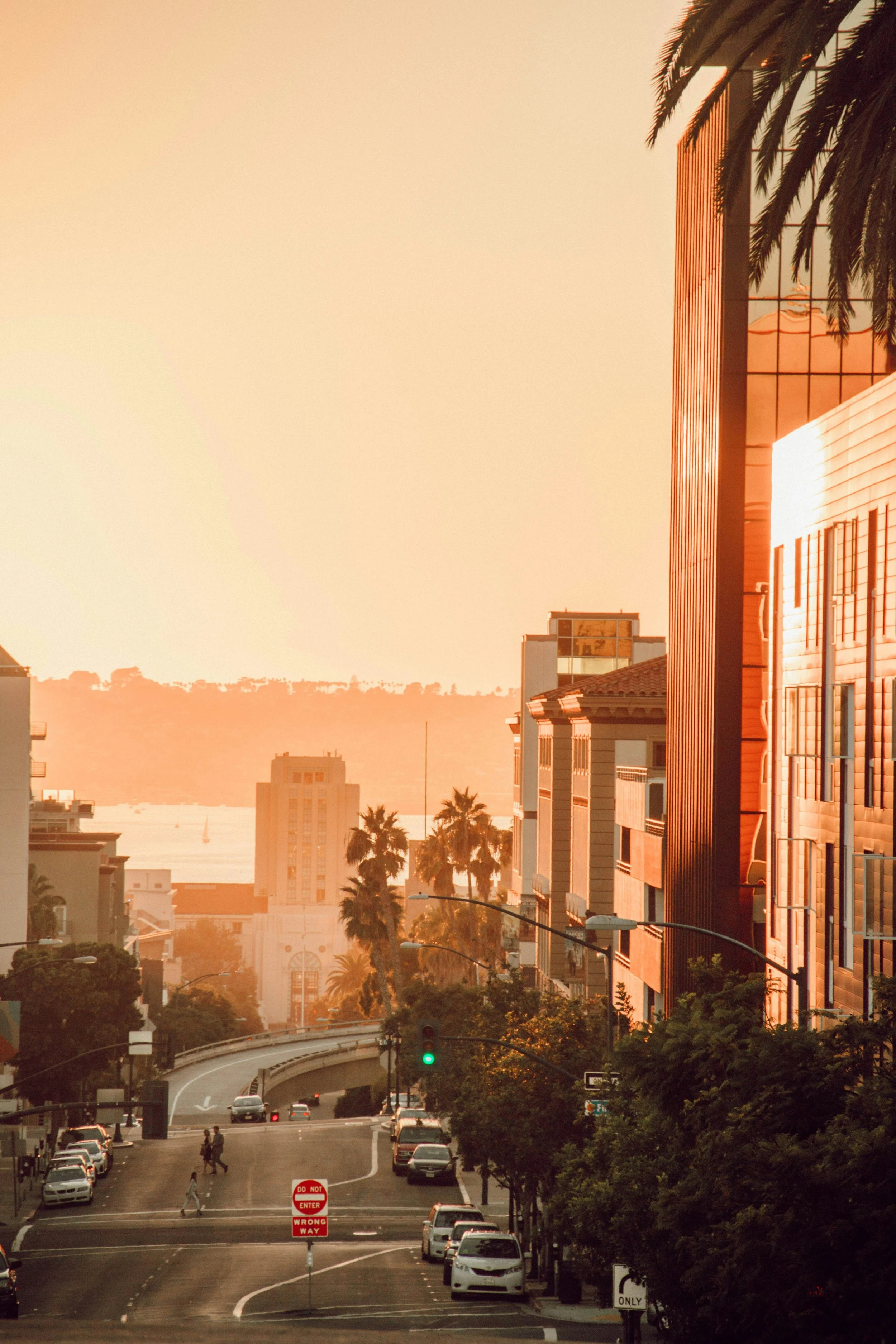 The soft orange light of a San Diego sunset fills a quiet street. The bay can seen at the end of the street, full of orange