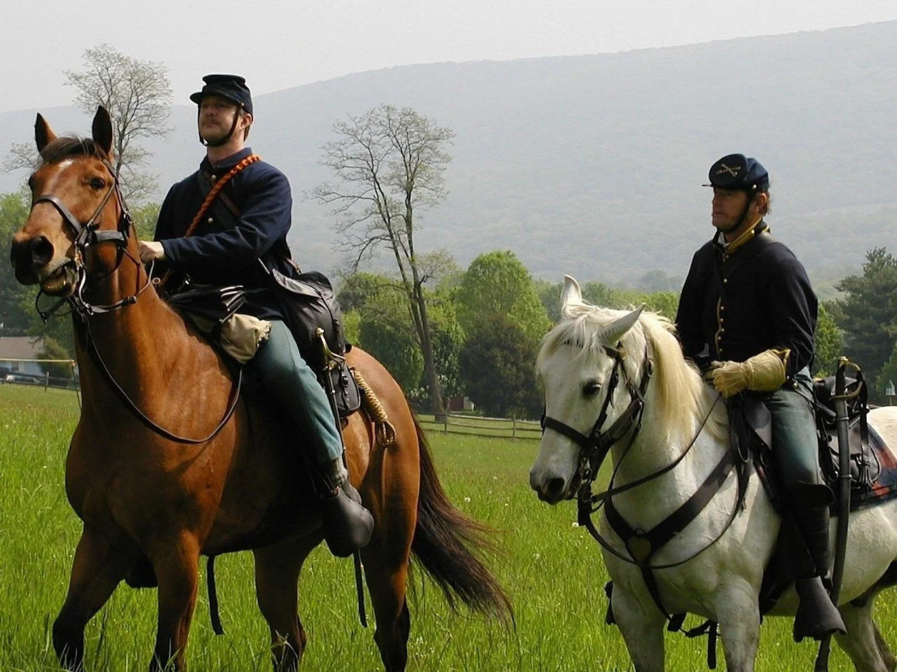 Two men dressed as Union soldiers ride their horses across a battlefield during a renactment. Drives & Detours Harpers Ferry history