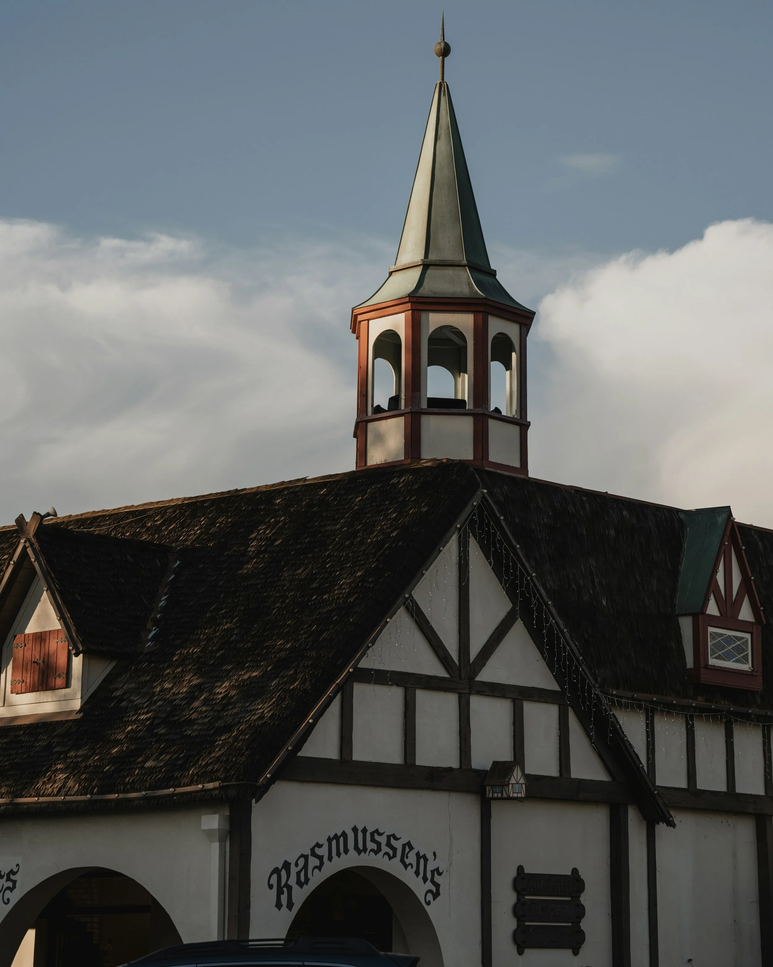 A tower stands over a white, timber-framed building in Solvang, California. It has the word: Rasmussen's written in gothic letters